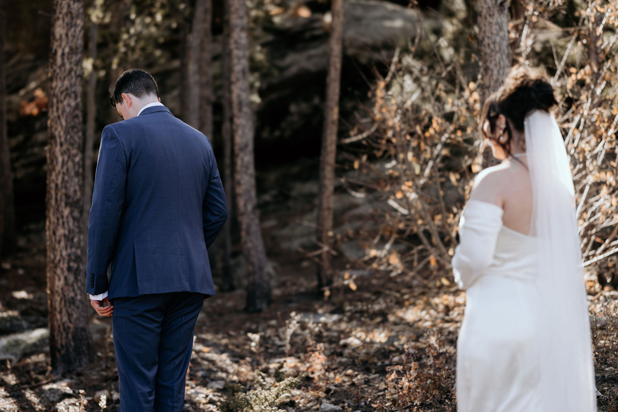 bride stands behind groom during elopement first look in the mountains