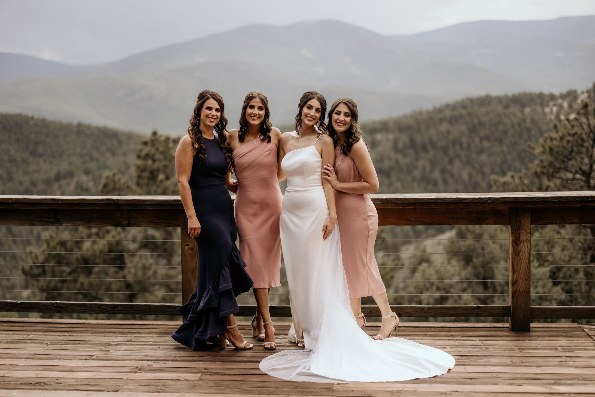 bride and bridesmaids stand on deck of colorado airbnb during mountain micro wedding.
