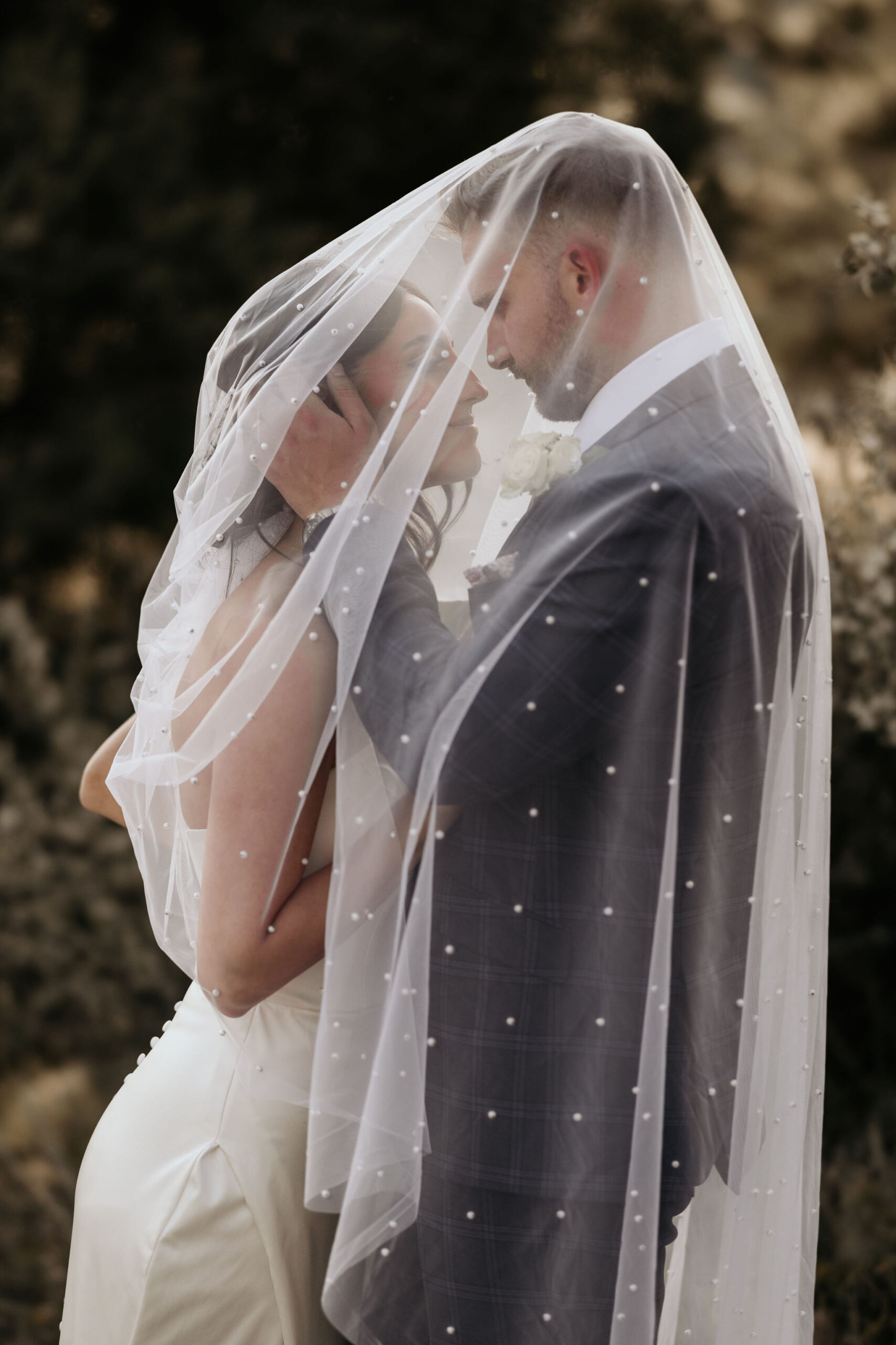 bride and groom smile at each other under wedding veil during mountain elopement