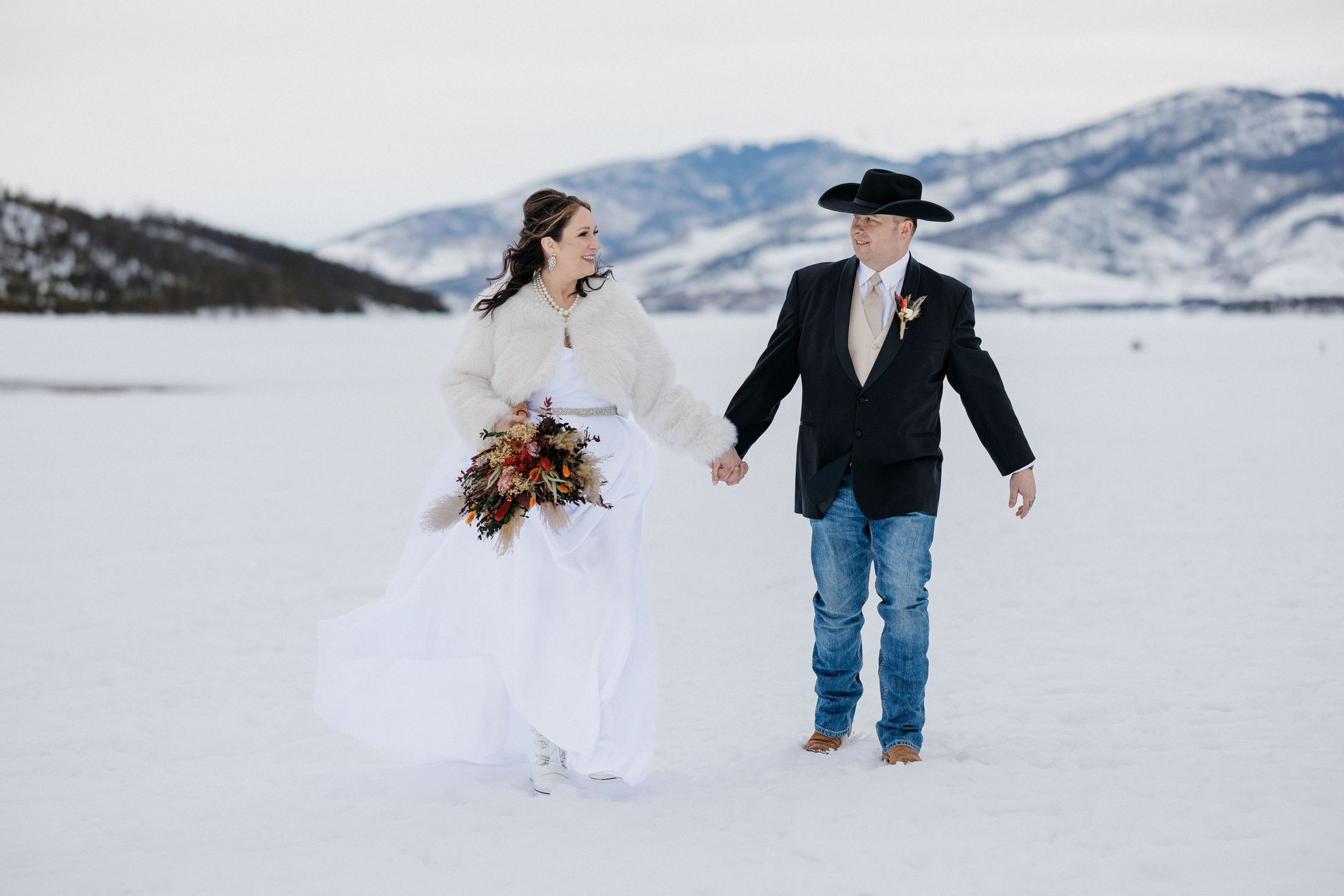 bride and groom hold hands and walk on frozen lake during colorado elopement
