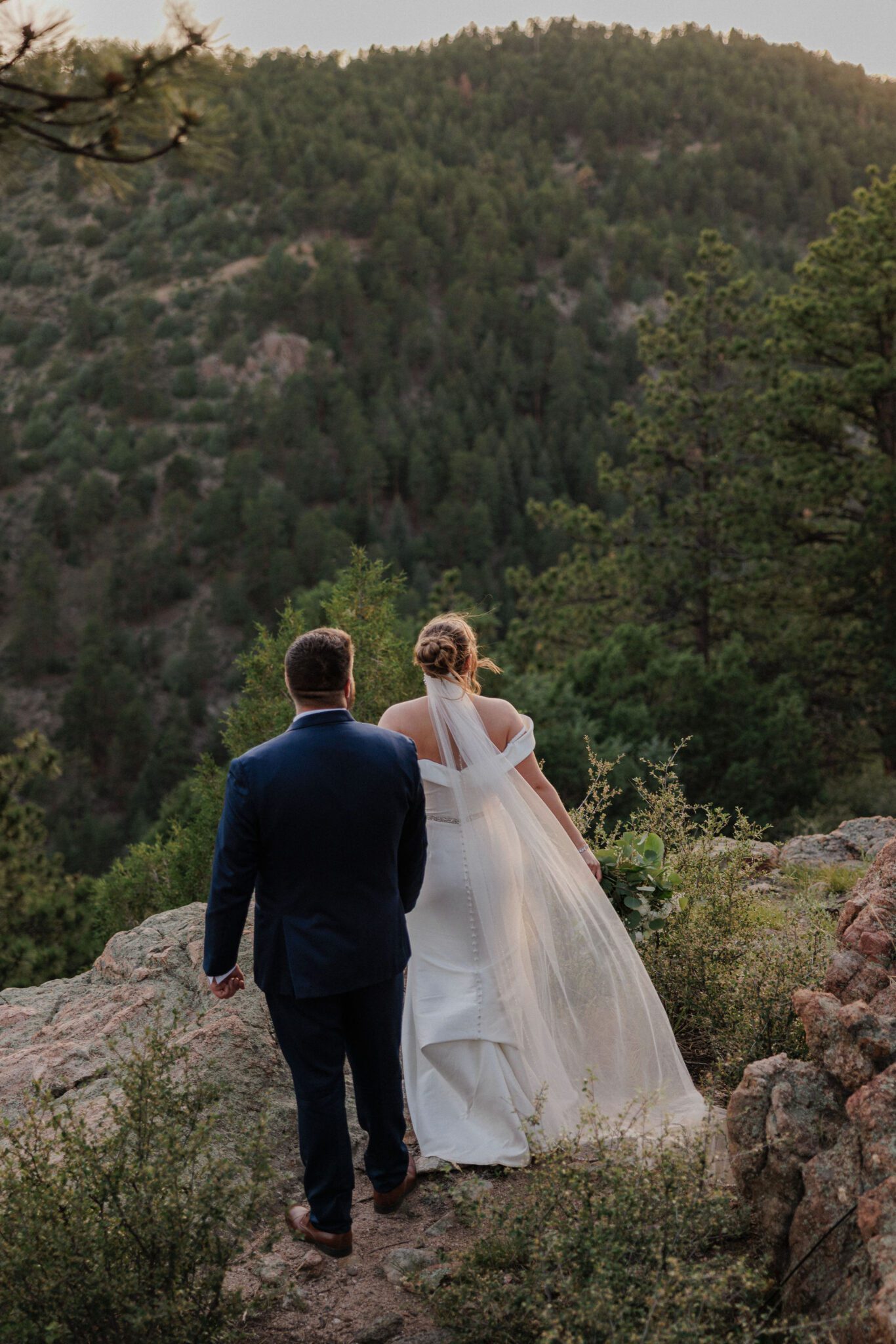 bride and groom hold hands and look out at the colorado mountains during dry wedding