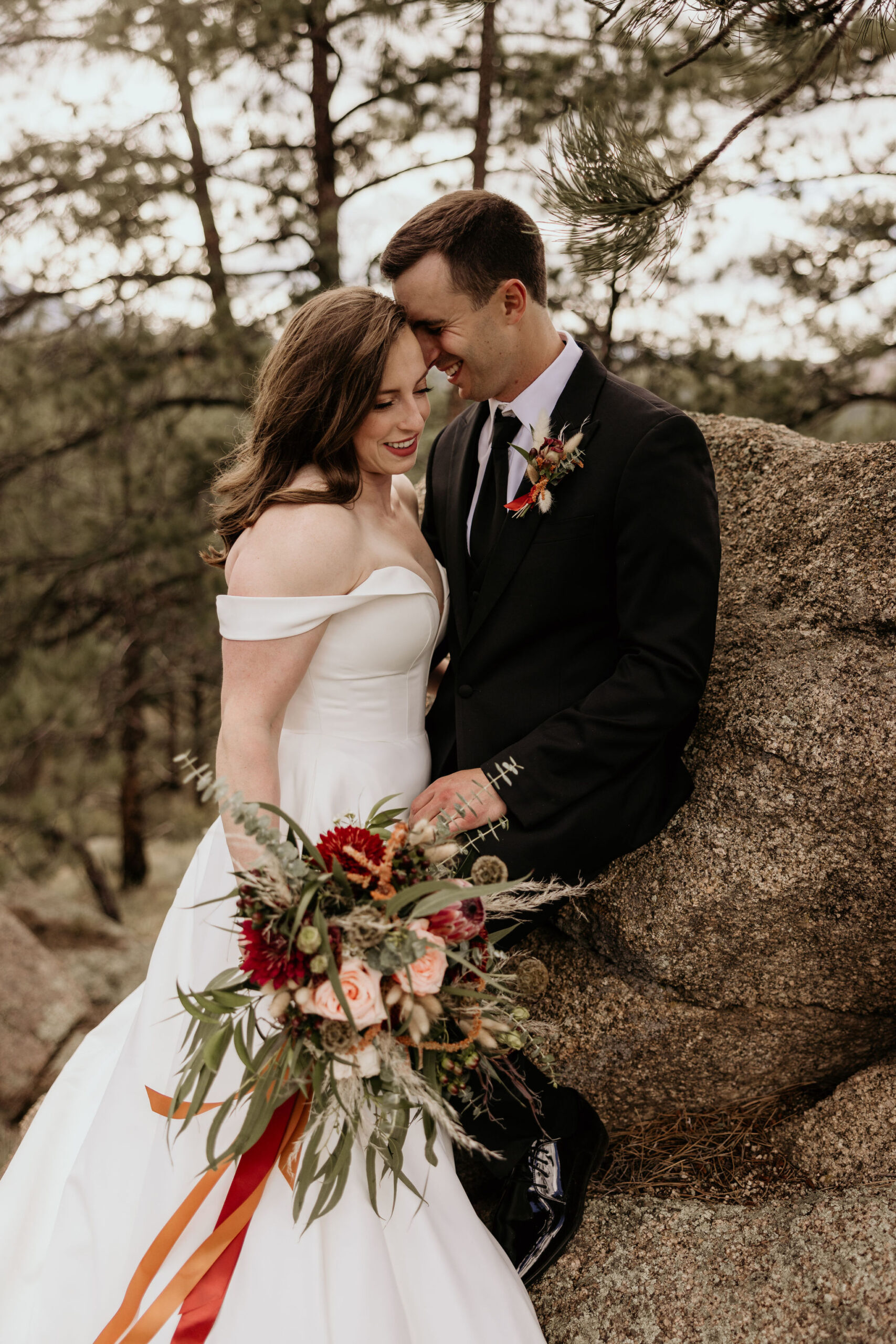 bride and groom lean on rock and smile after they tell their family about their elopement.