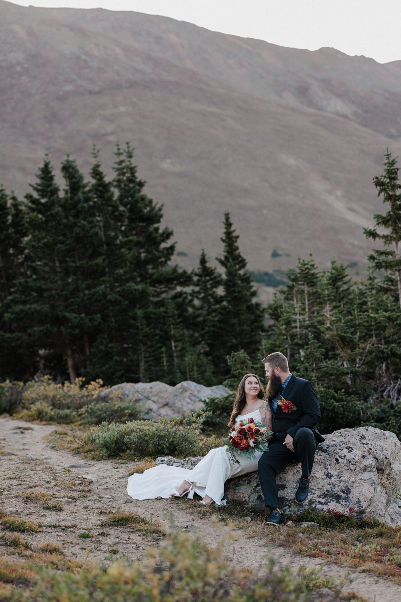 bride and groom sit on rock with trees surrounding them during elopement photos