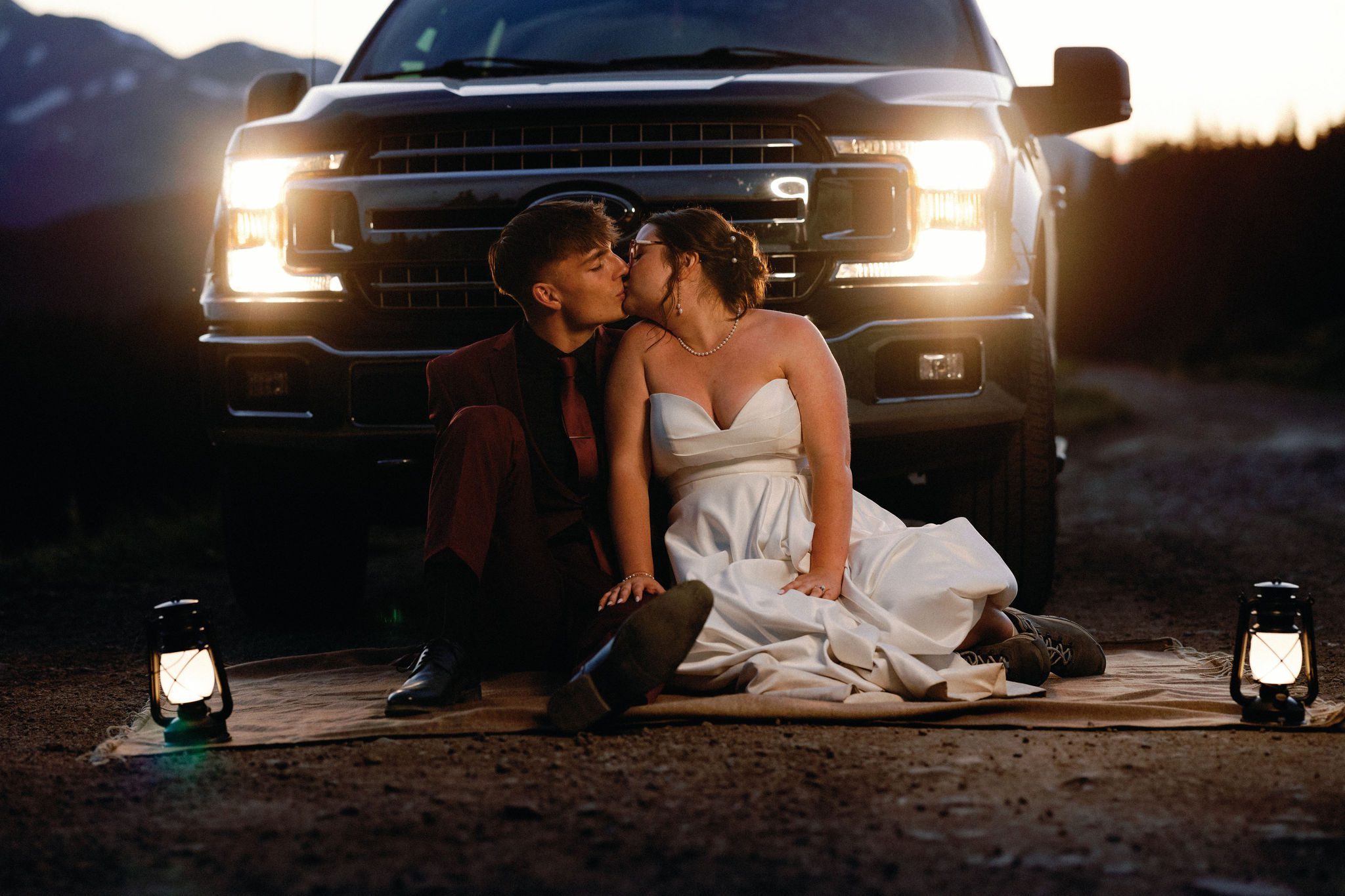 after telling family they eloped, bride and groom sit on blanket in front of truck with its lights on