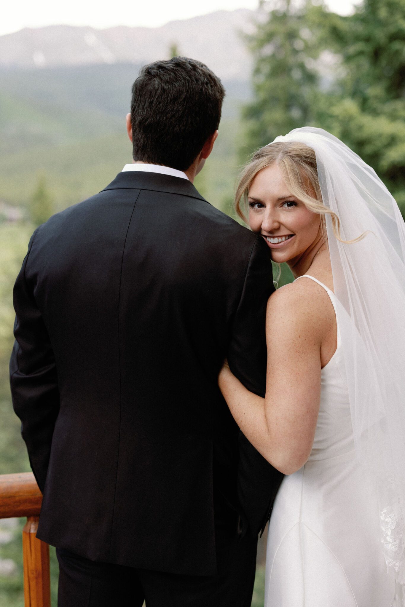 bride looks at camera and leans head on grooms shoulder during their vow renewal in colorado at an airbnb