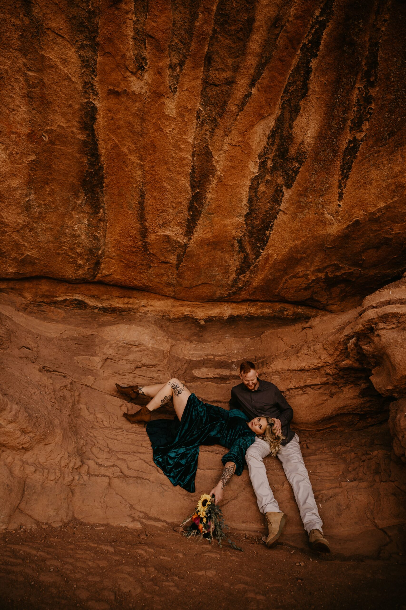 engaged couples sits on red rocks with flowers during engagement photos