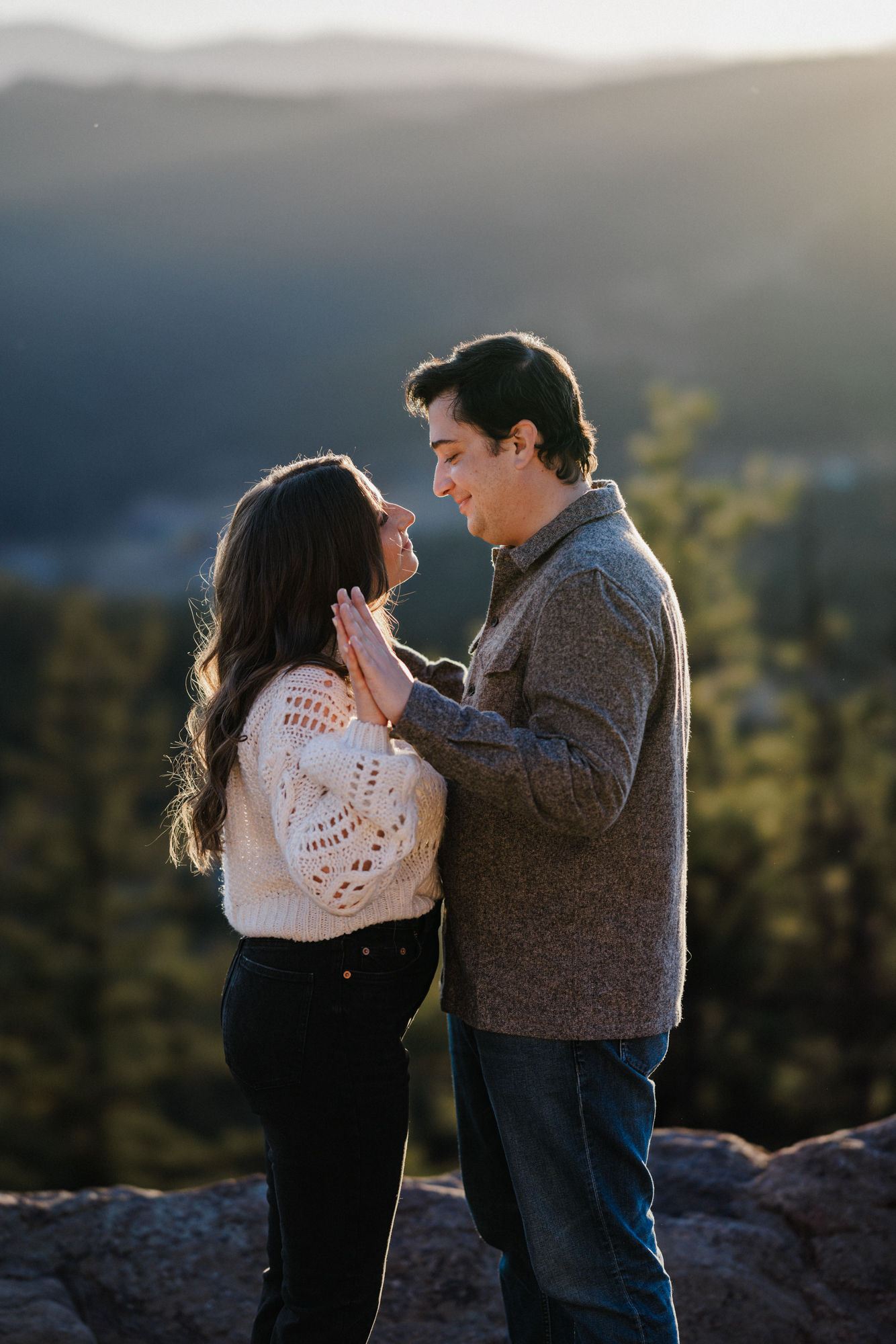 engaged couple stands on rock during sunset engagement photos in colorado