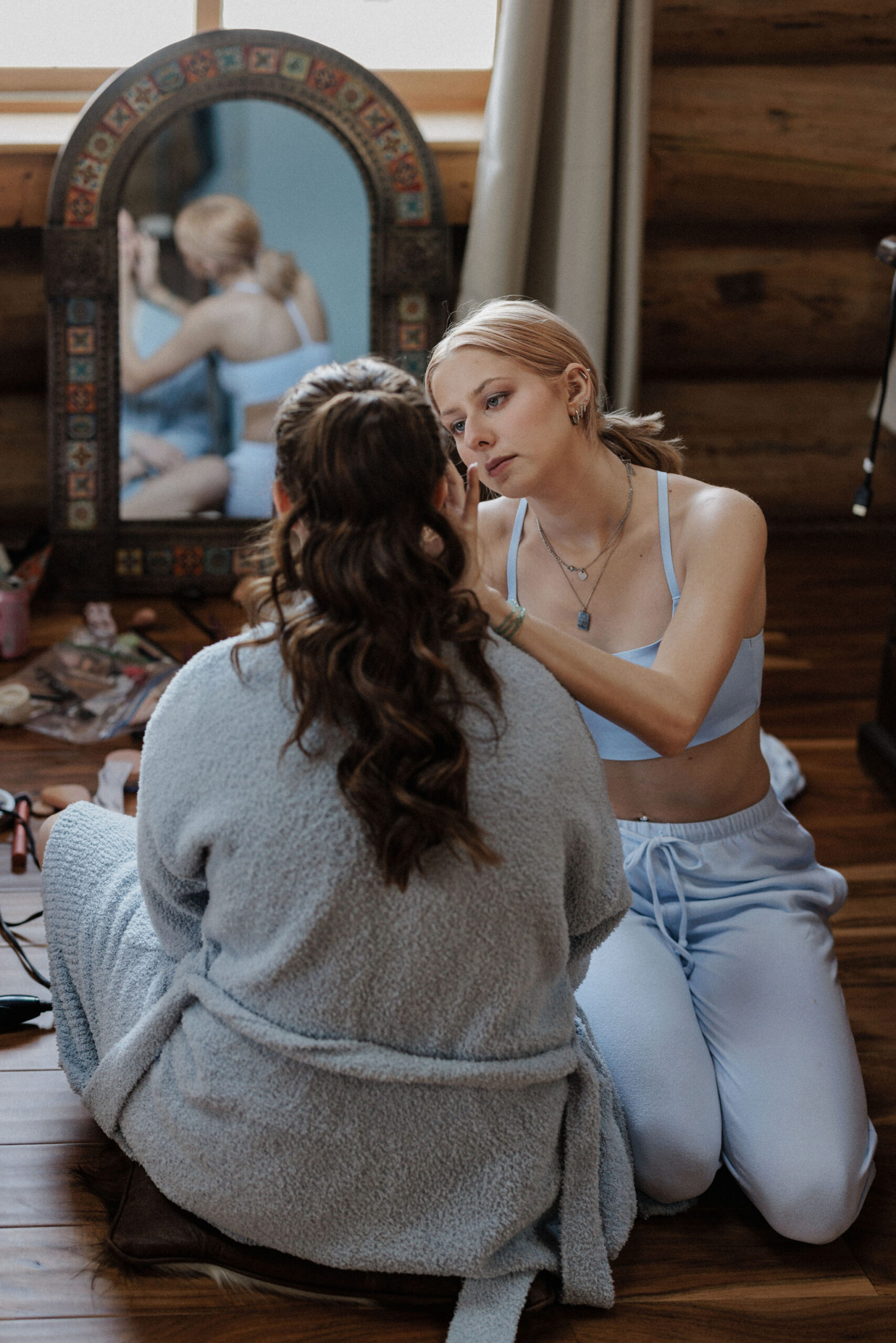 bridesmaid helps bride do hair and makeup during getting ready photos