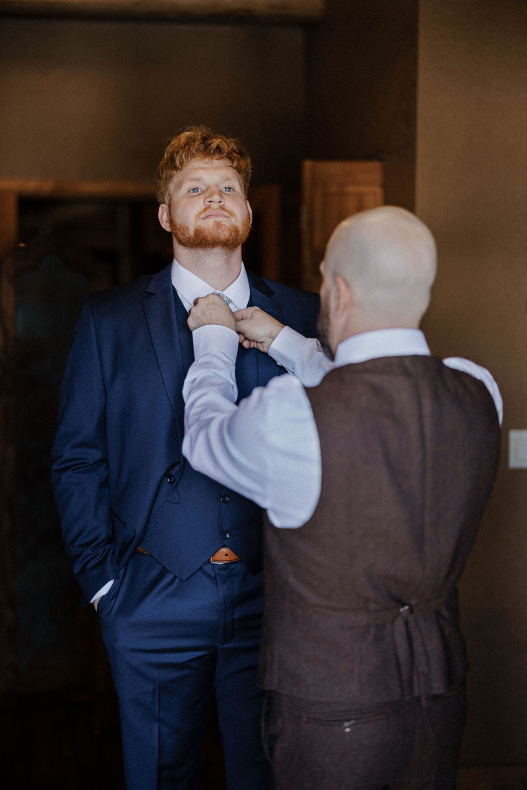 father of the bride helps groom put on tie in airbnb