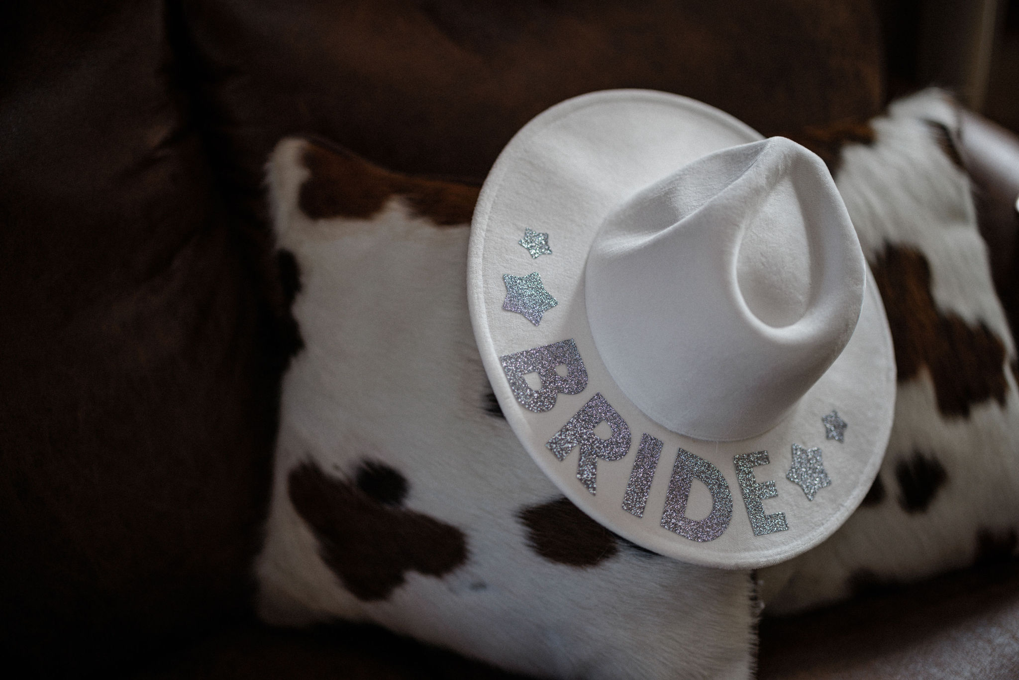 white cowboy hat with 'bride' on it sits on cow hide pillow for western wedding in colorado.