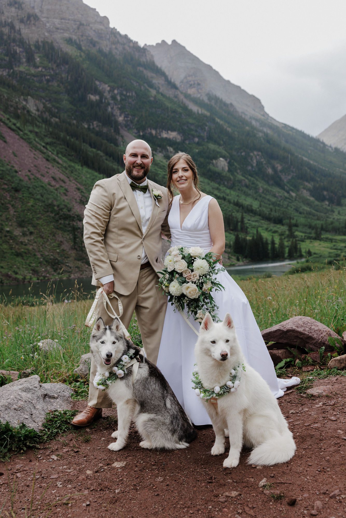 Bride and groom stand at maroon bells with their two pups during their colorado elopement with dogs