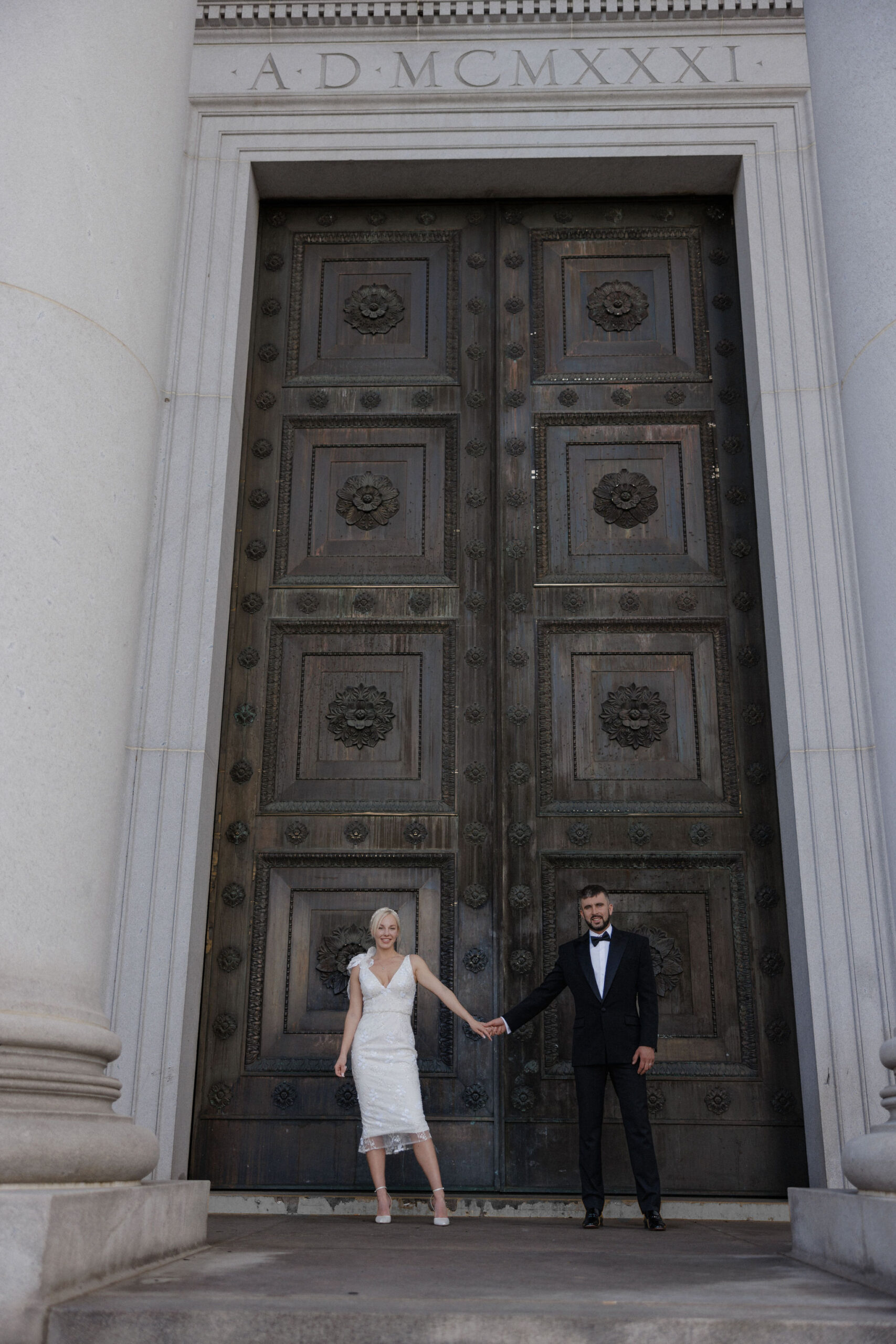 bride and groom hold hands and stand in front of big wooden door during elopement photos at colorado courthouse