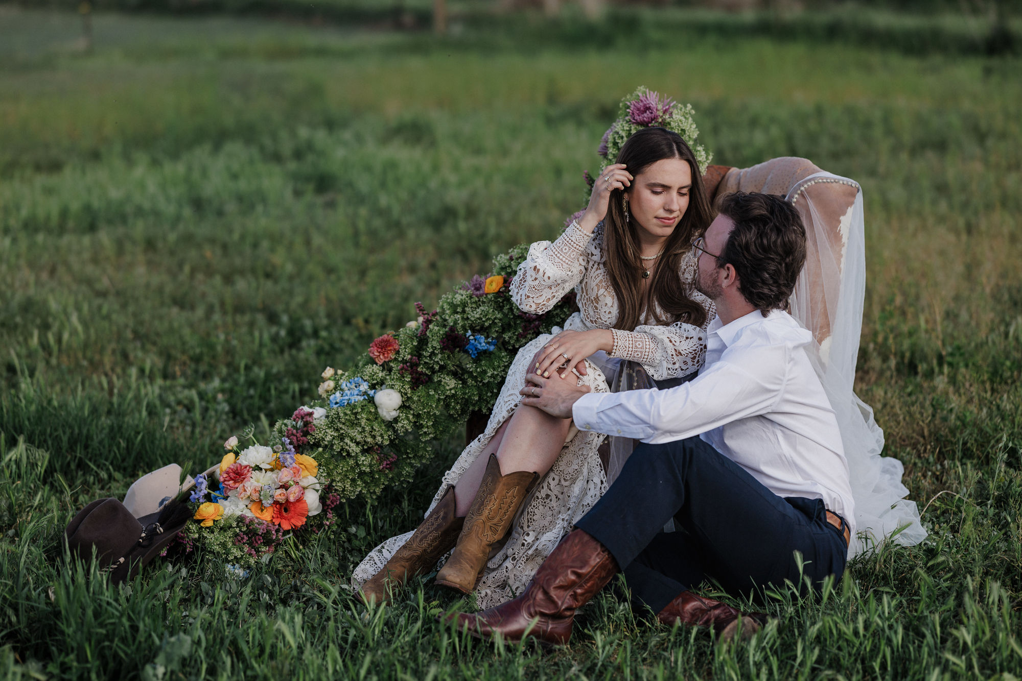 bride and groom sit in chair surrounded by flowers during wedding photos