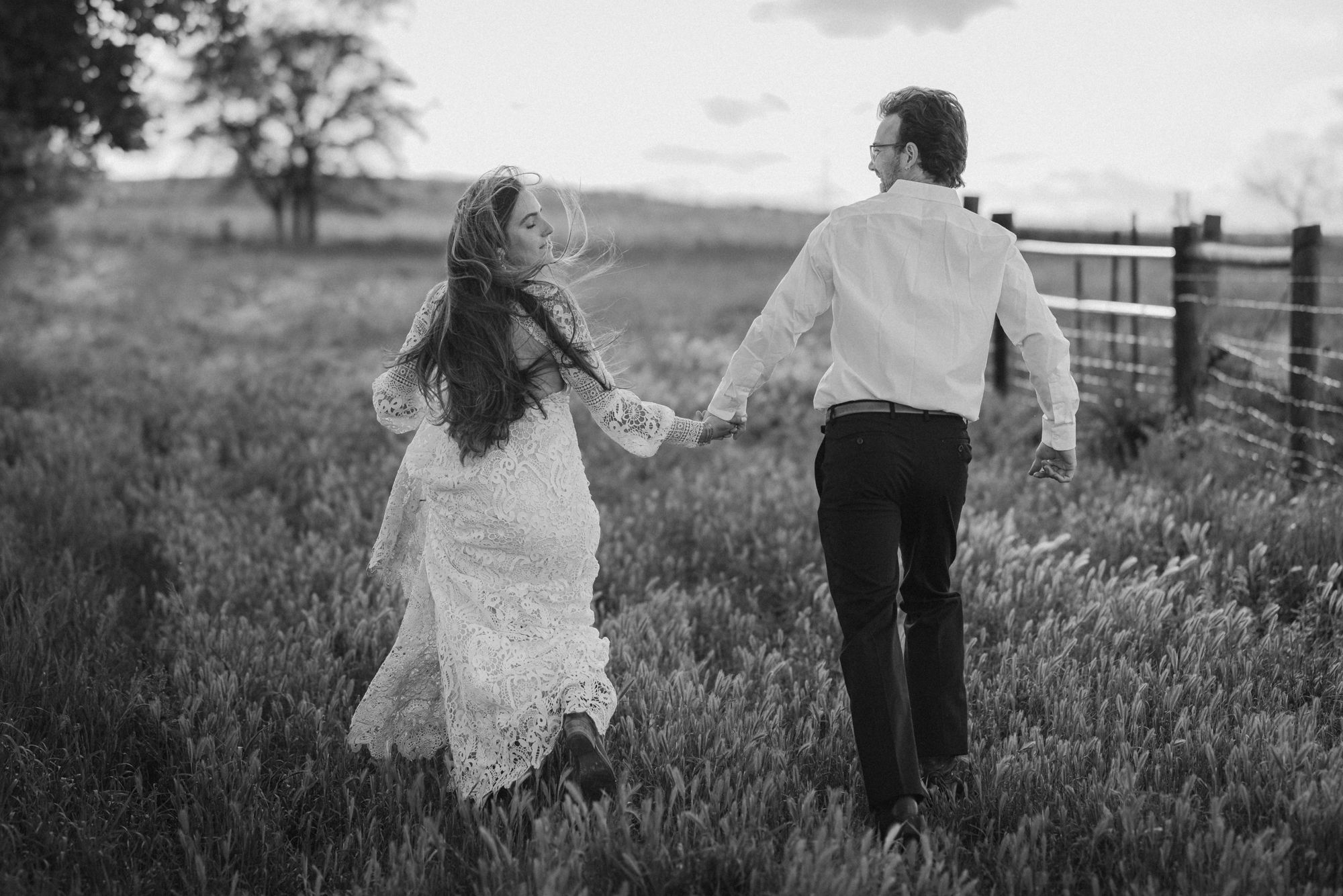 bride and groom hold hands and run through field in colorado