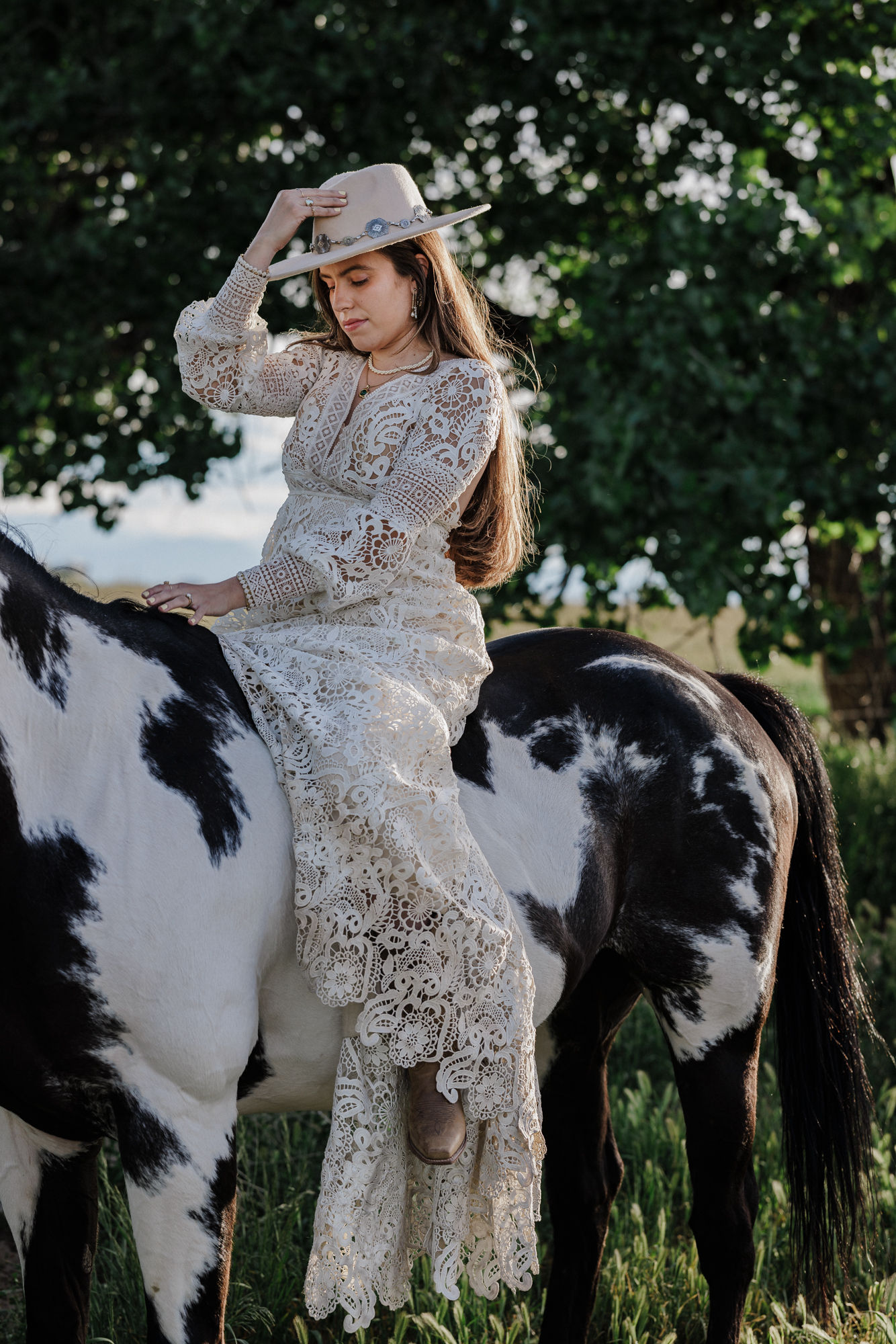 bride holds cowboy hat on her head while sitting on a horse during bridal photos at colorado elopement