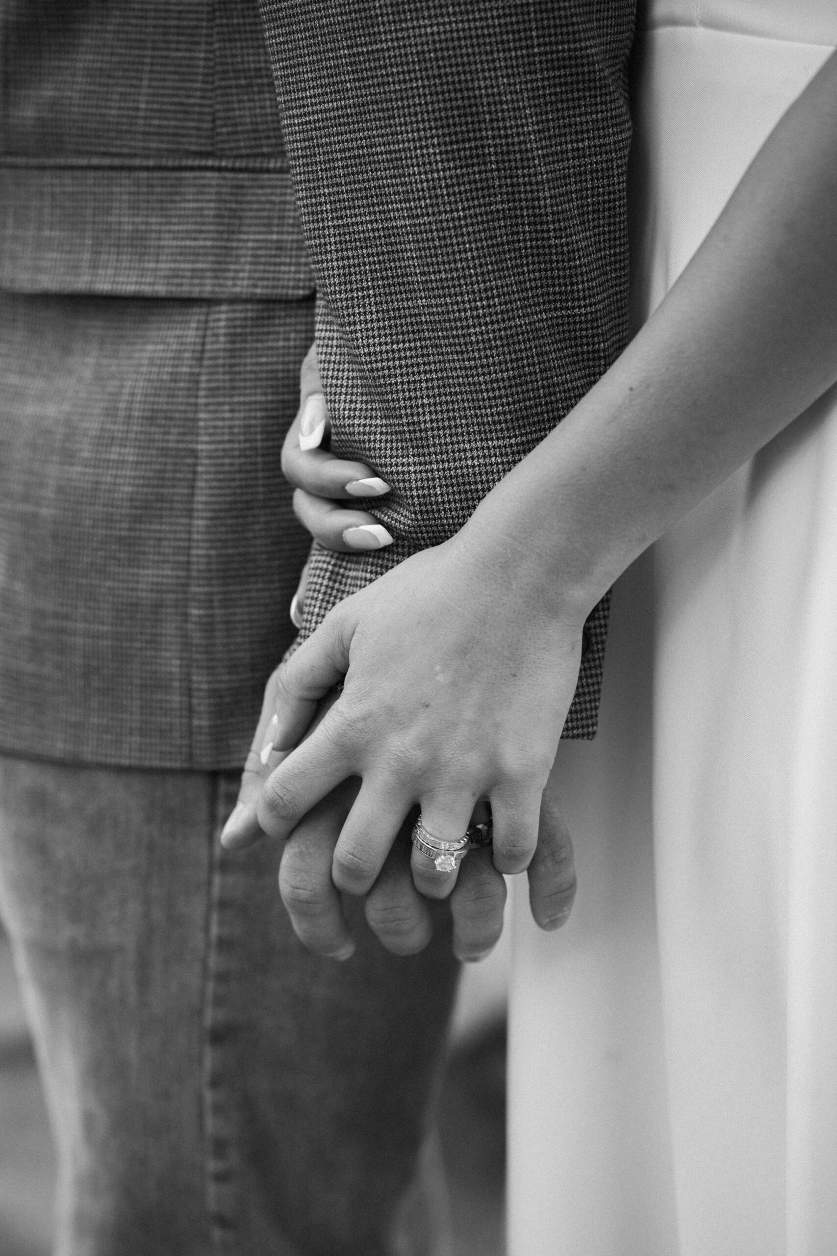 close up image of bride and groom holding hands with wedding ring