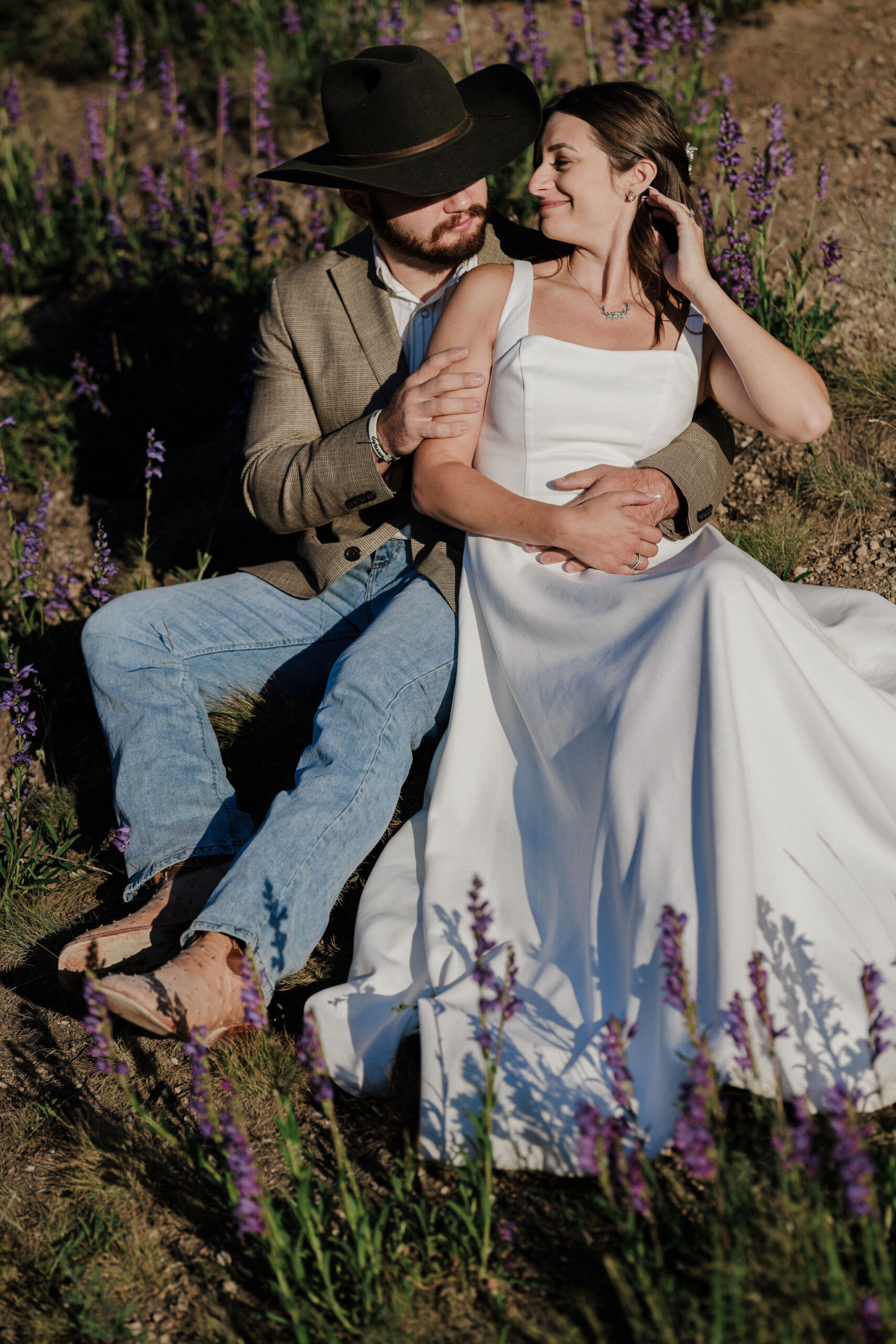 bride and groom sit on ground as they hold each other and smile