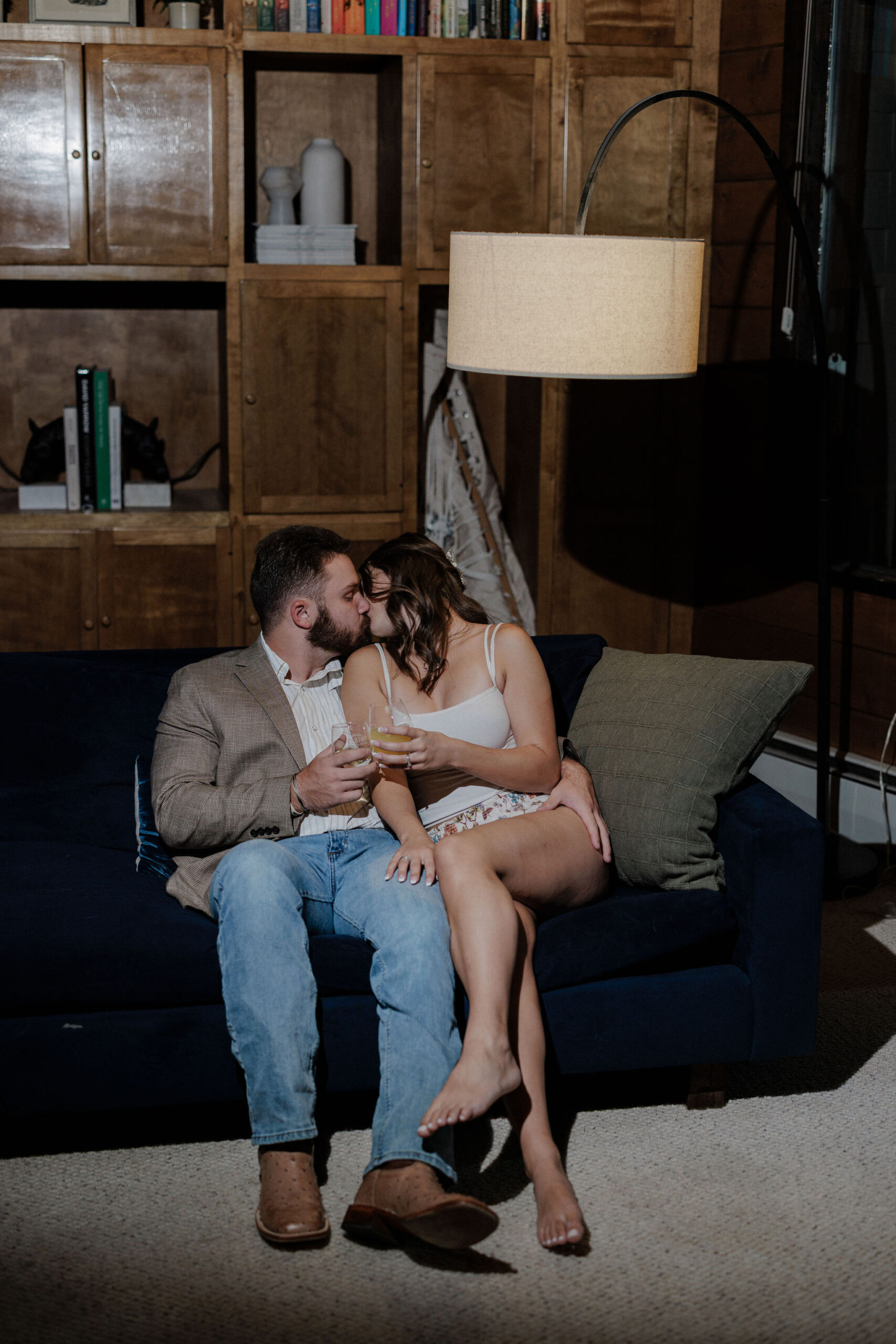 bride and groom sit on couch and kiss while getting ready for their wedding