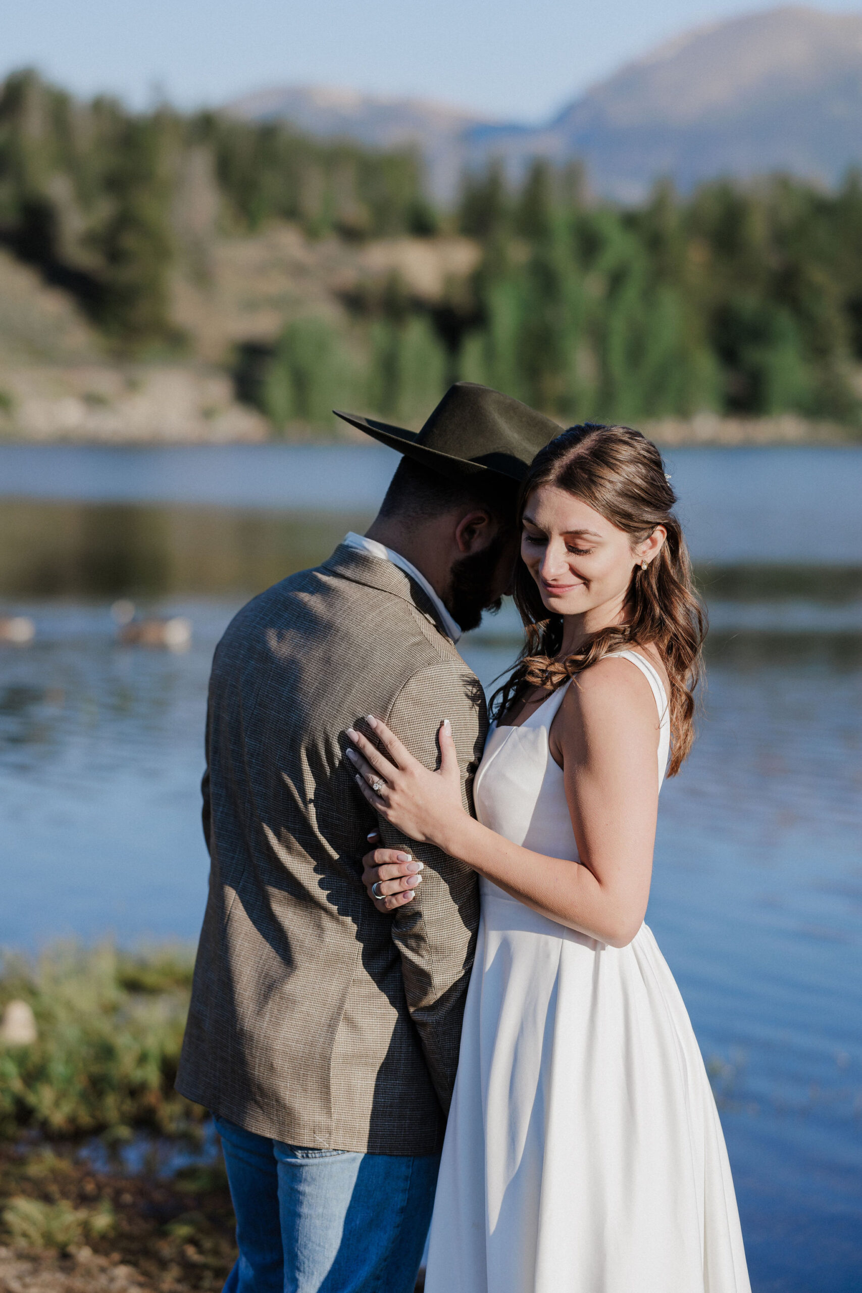 bride holds onto grooms arm beside lake dillon as they take elopement photos