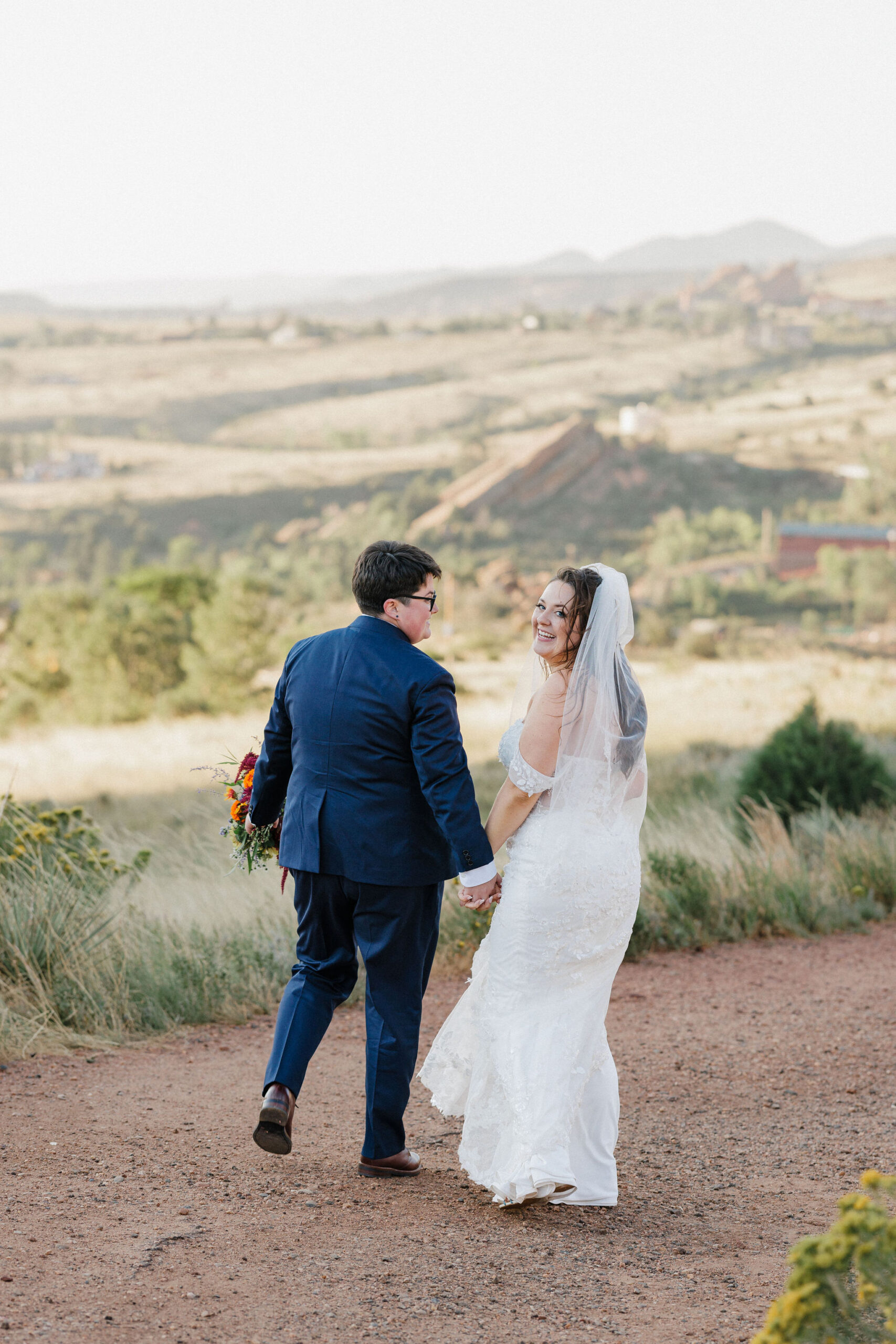 two brides hold hands and walk along trail at red rocks park