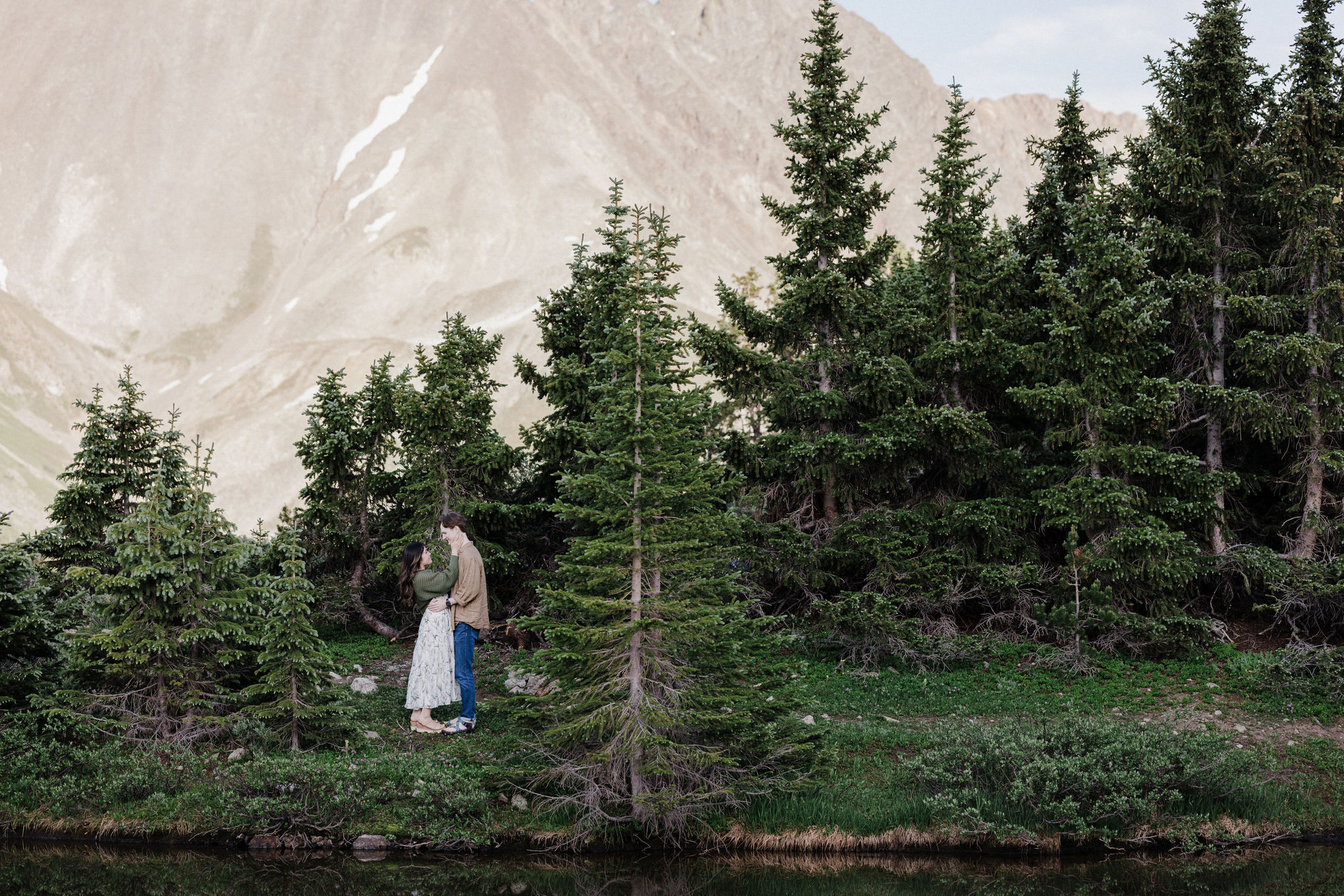 man and woman stand on edge of pass lake in Breckenridge during engagement photos