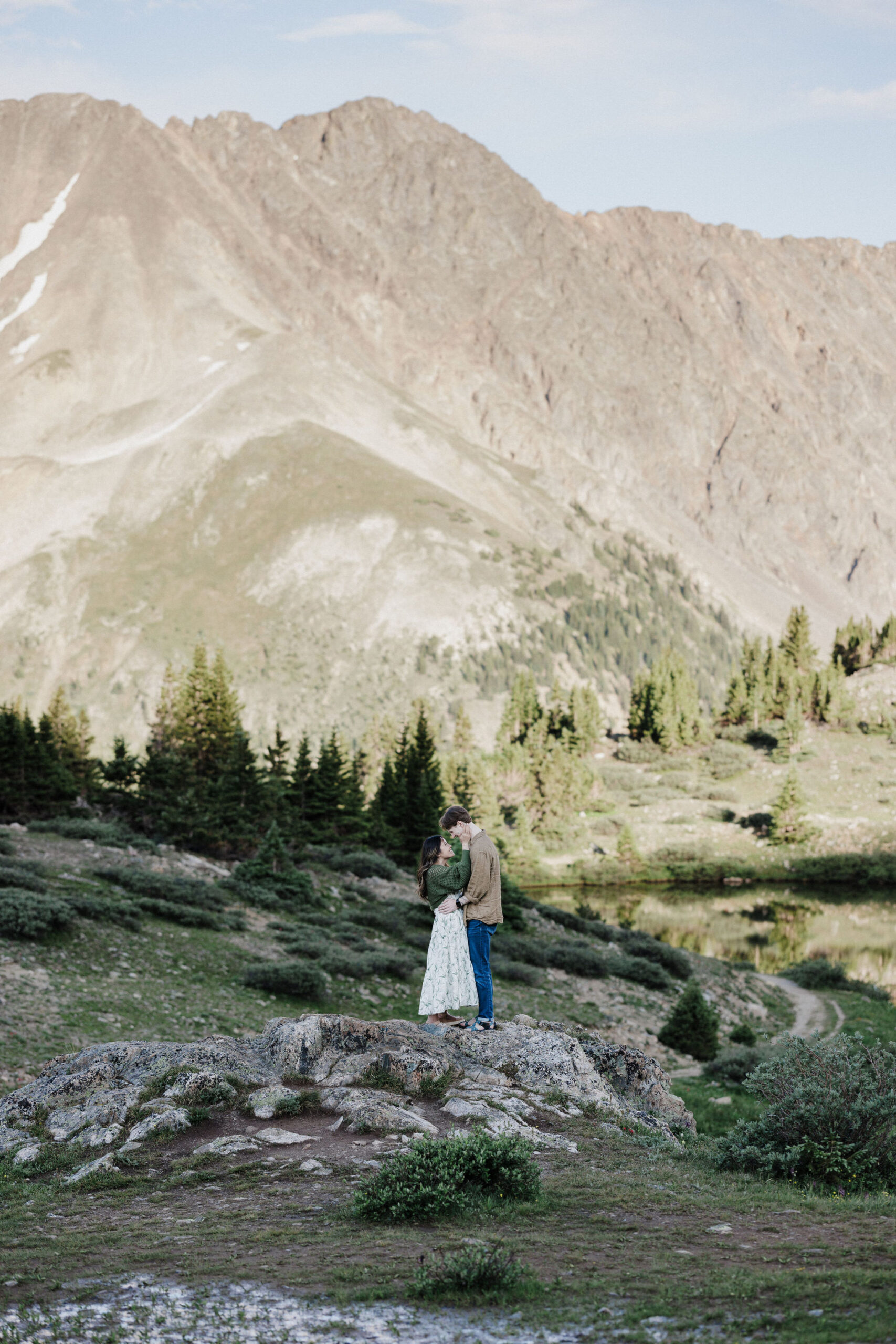 engaged couple stands on rock at pass lake during engagement photos