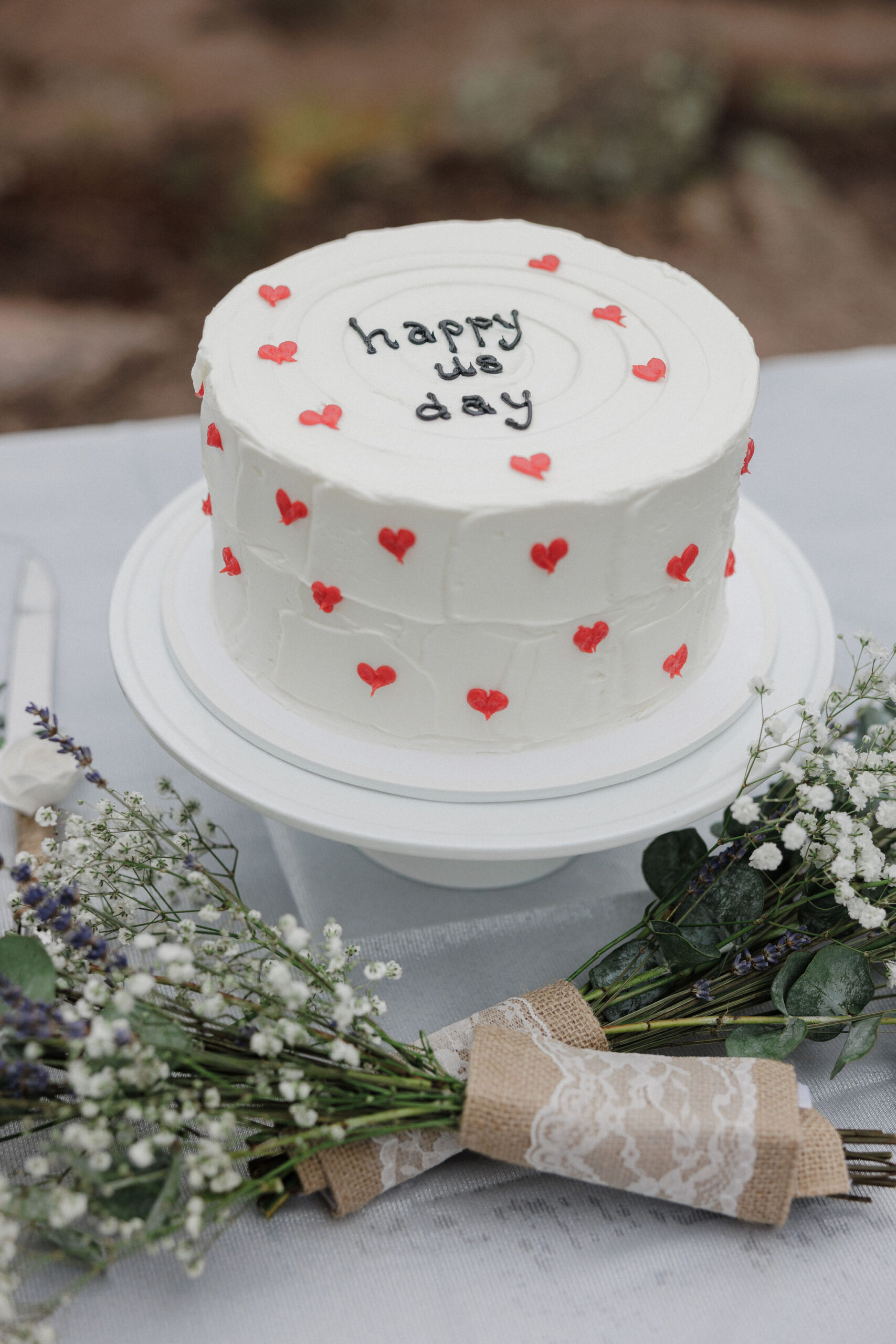 close up of white elopement cake with little red hearts and wordsthat say "happy us day"