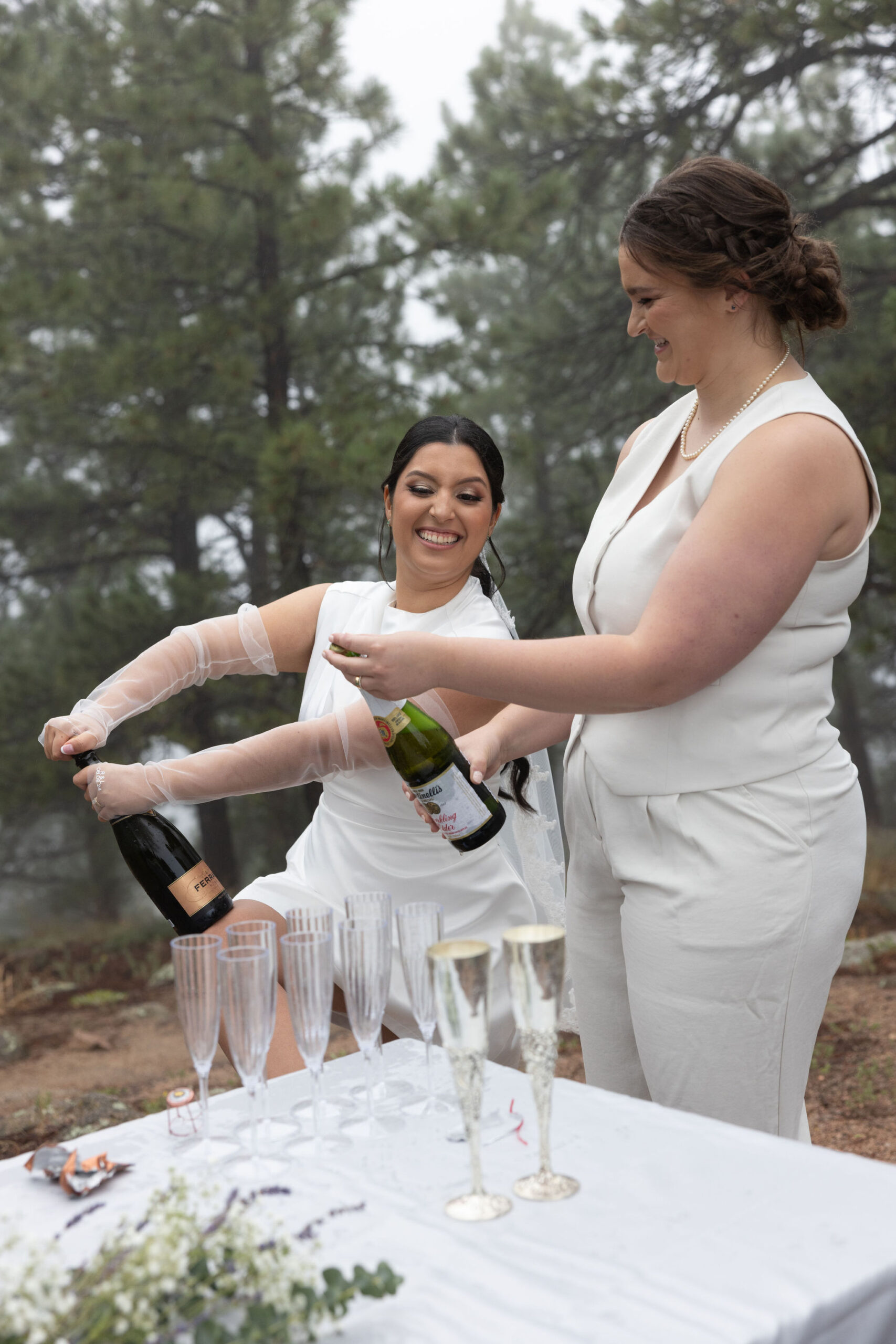 two brides open bottles of champagne