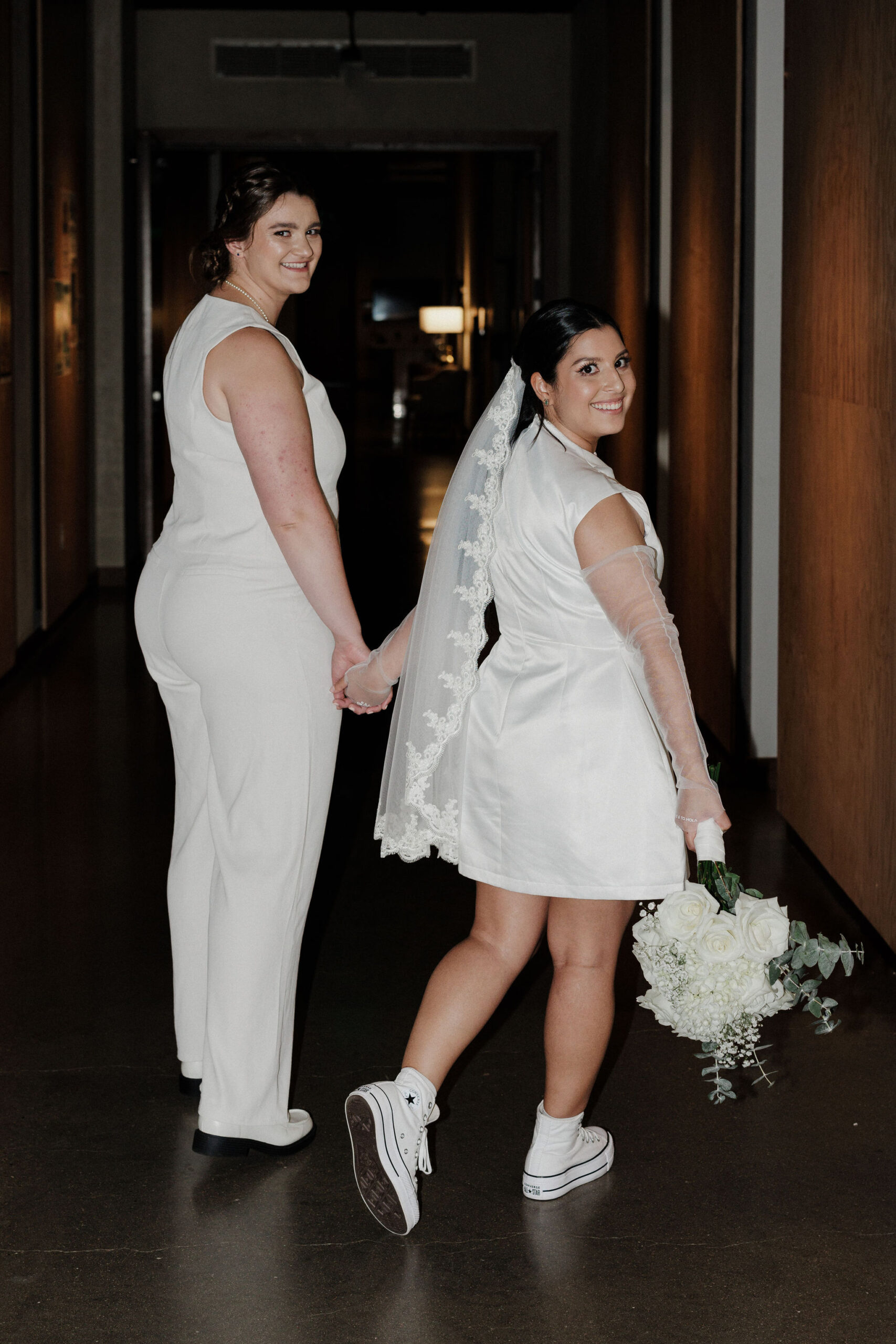 two brides hold hands as they walk down hallway during elopement in boulder