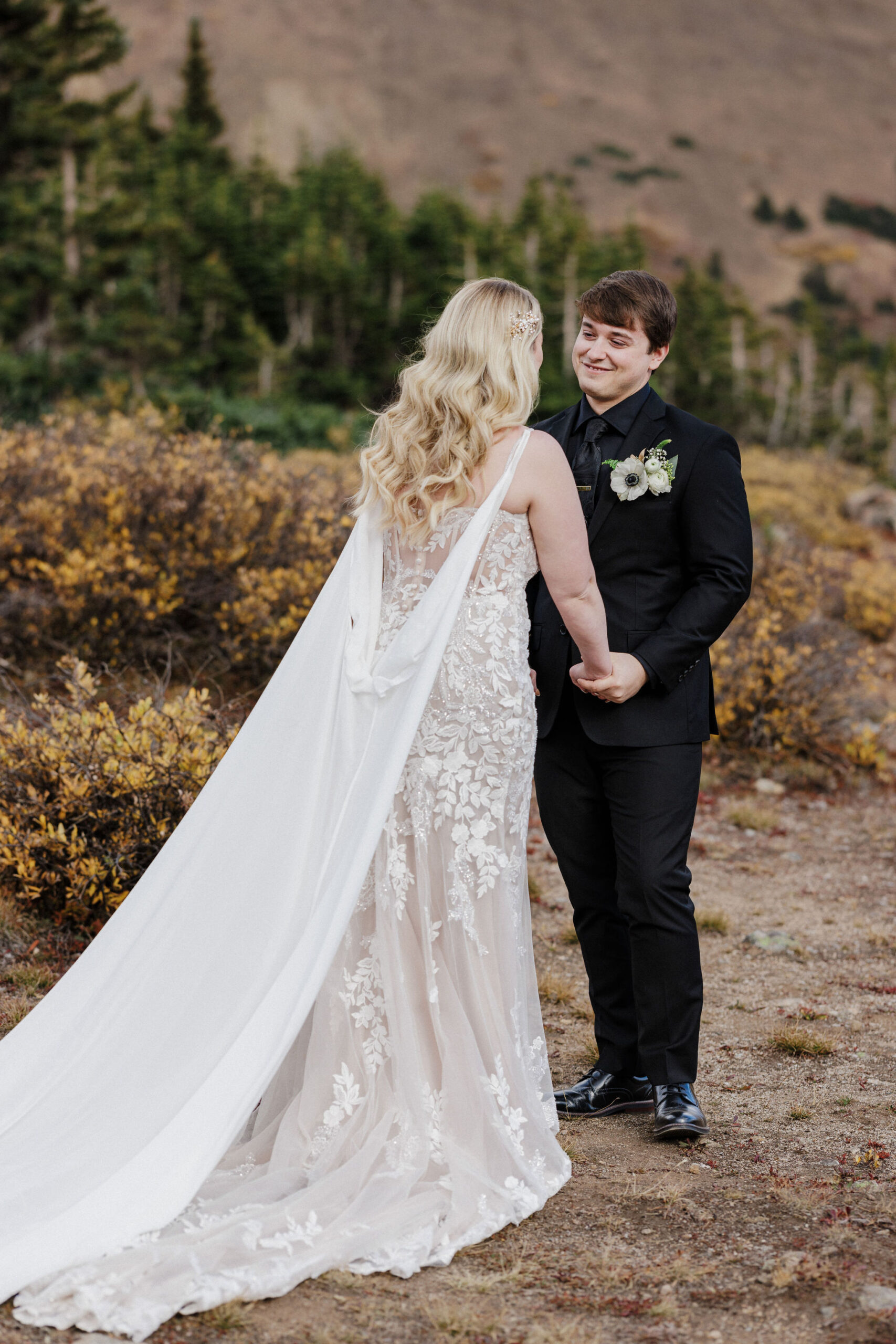 bride and groom smile at each other, holding hands during wedding day first look