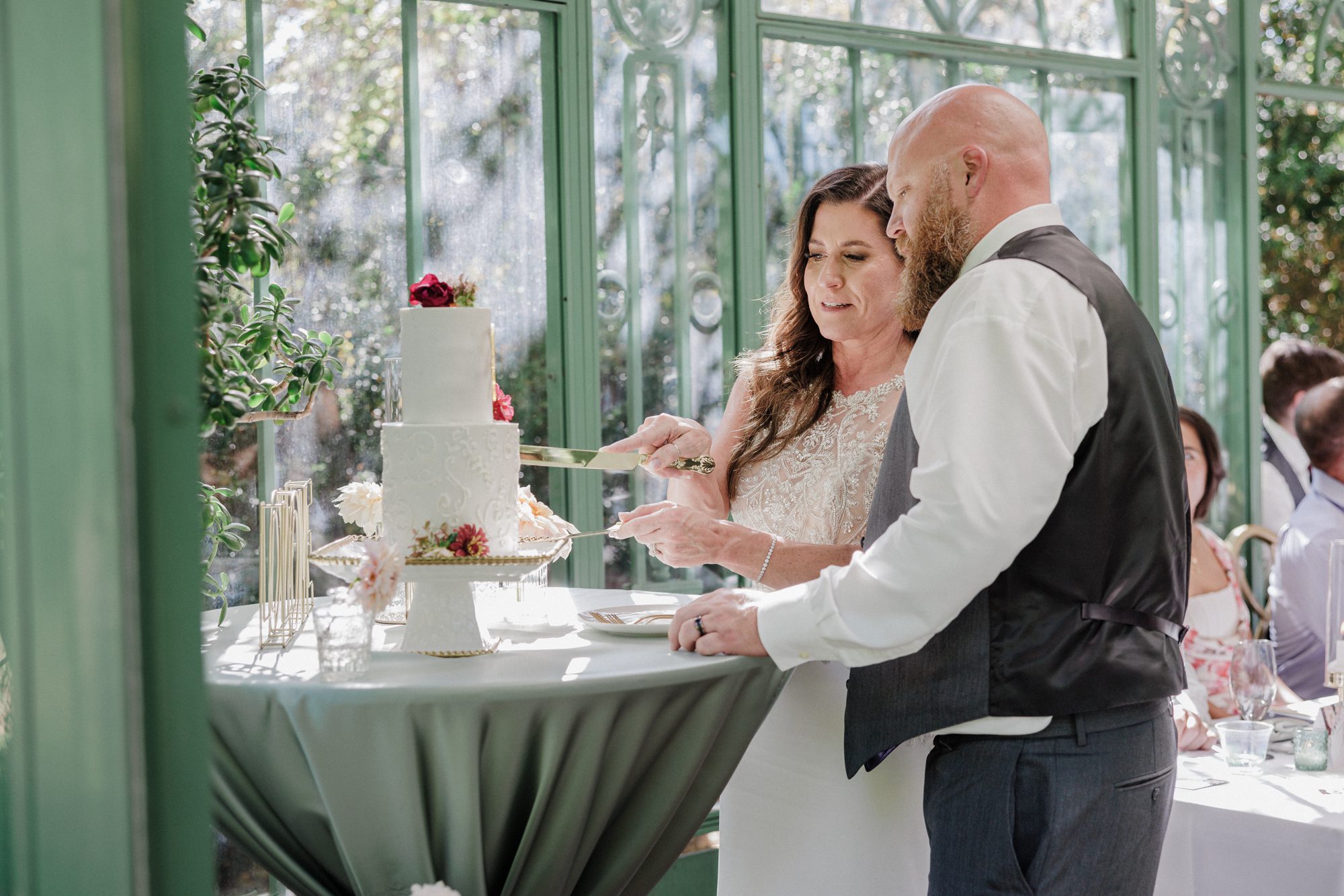 Bride and groom cut cake during Denver Botanic Garden solarium wedding.