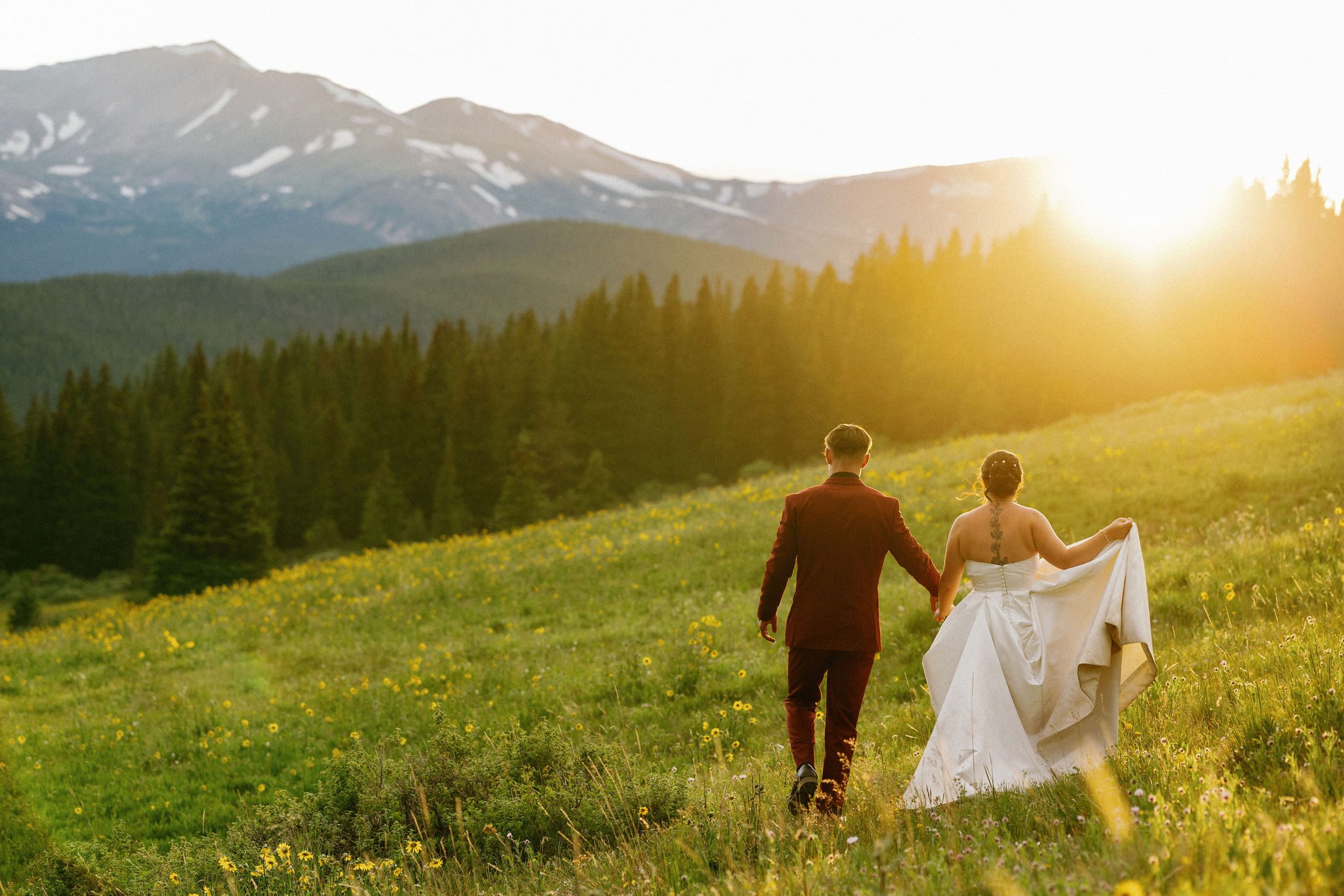 bride and groom hold hands and walk through the grassy areas around the colorado mountains