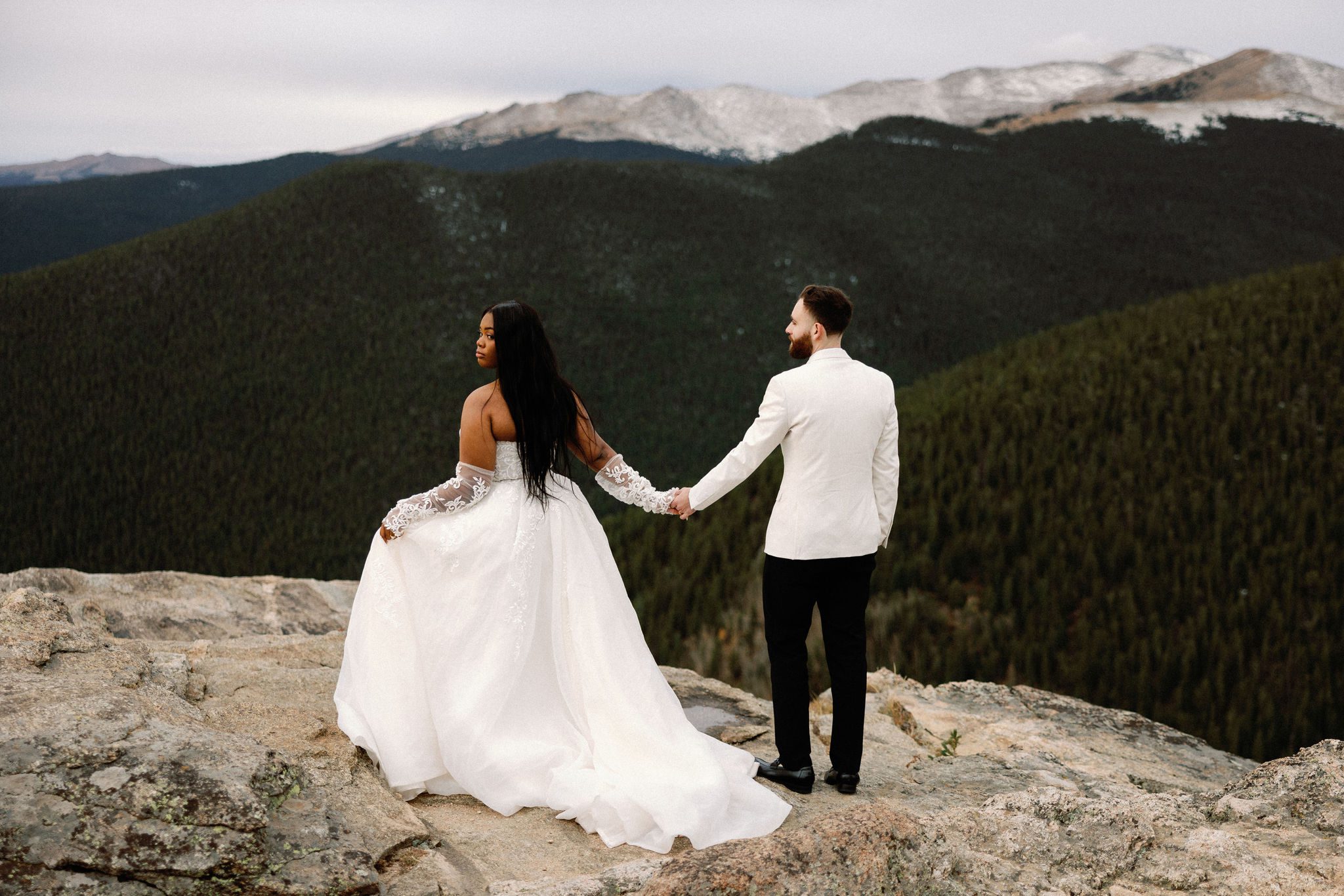 bride and groom stand on rock overlooking the mountains after asking 'should i elope or have a wedding'
