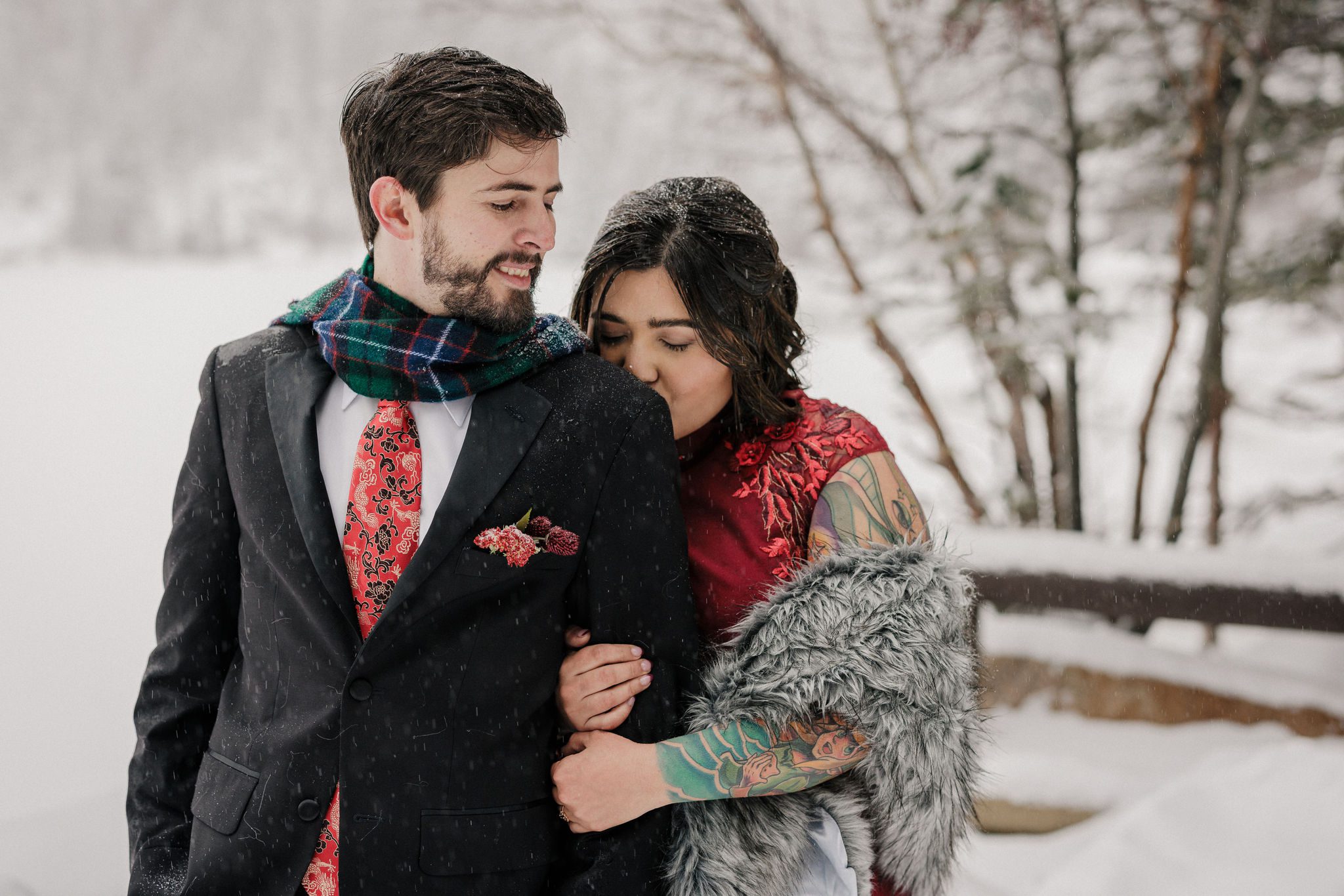 bride kisses grooms shoulder while taking winter elopement photos