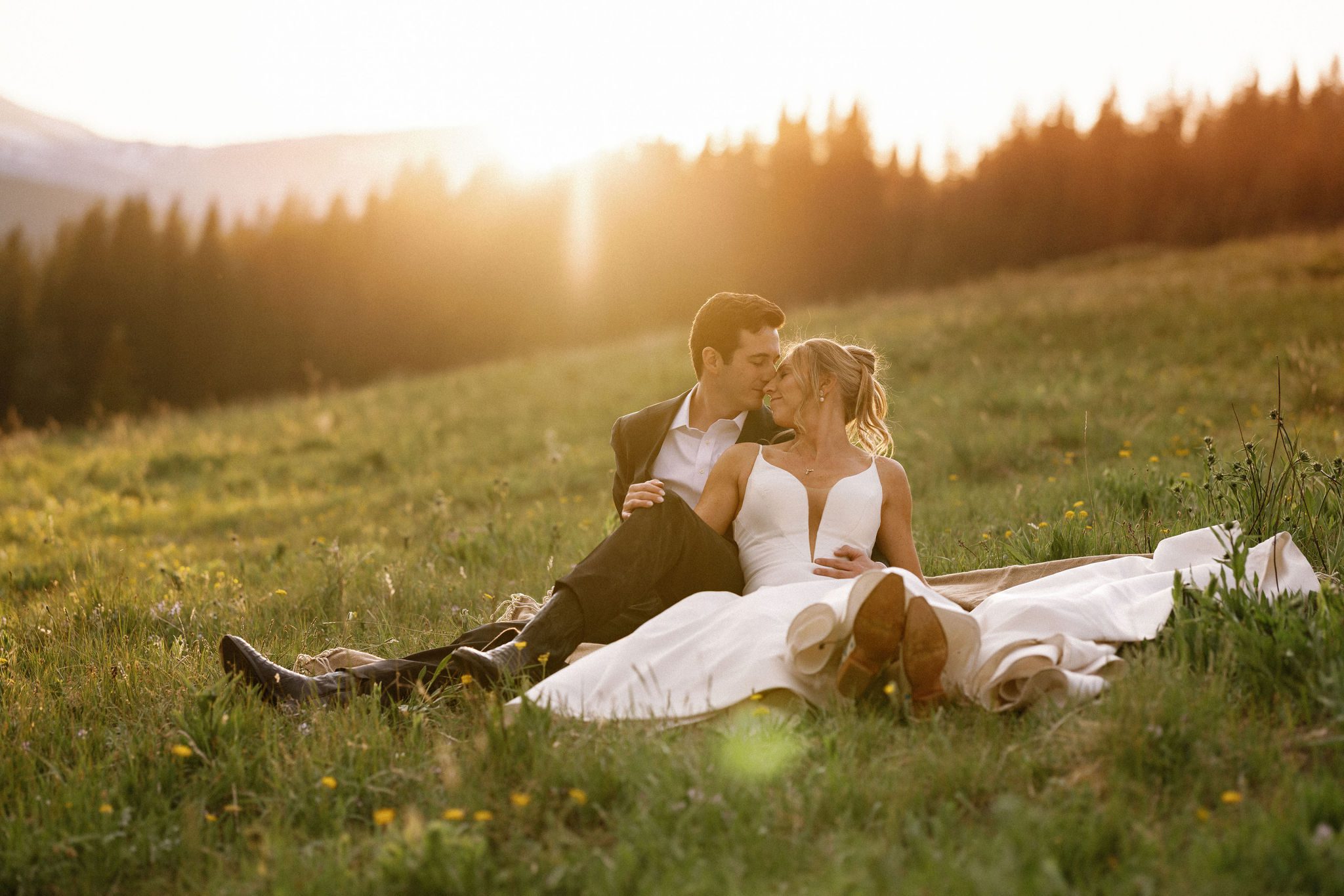 bride and groom sit on grassy area in the colorado mountains during wedding photos