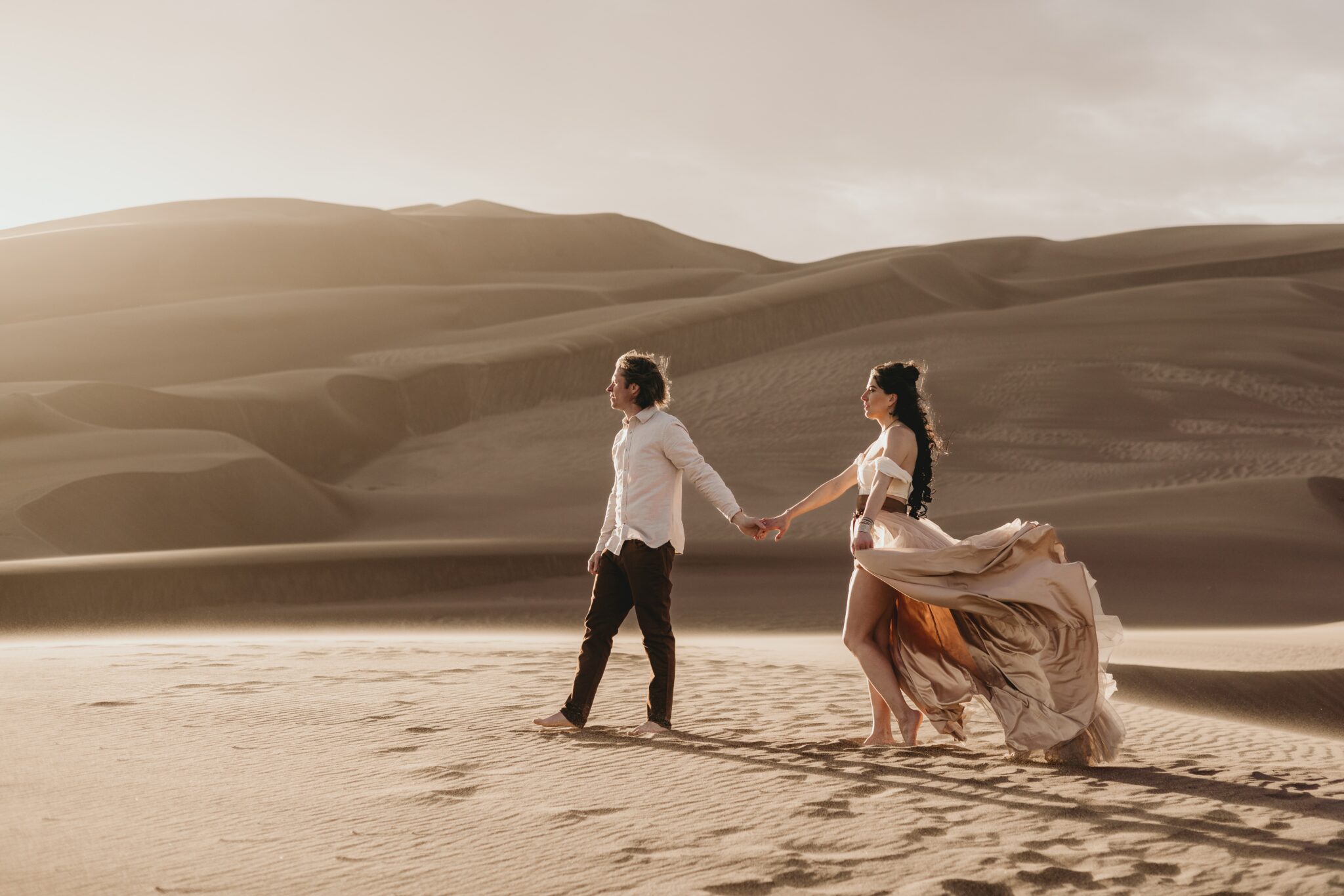 bride and groom hold hands and walk in the sand dunes