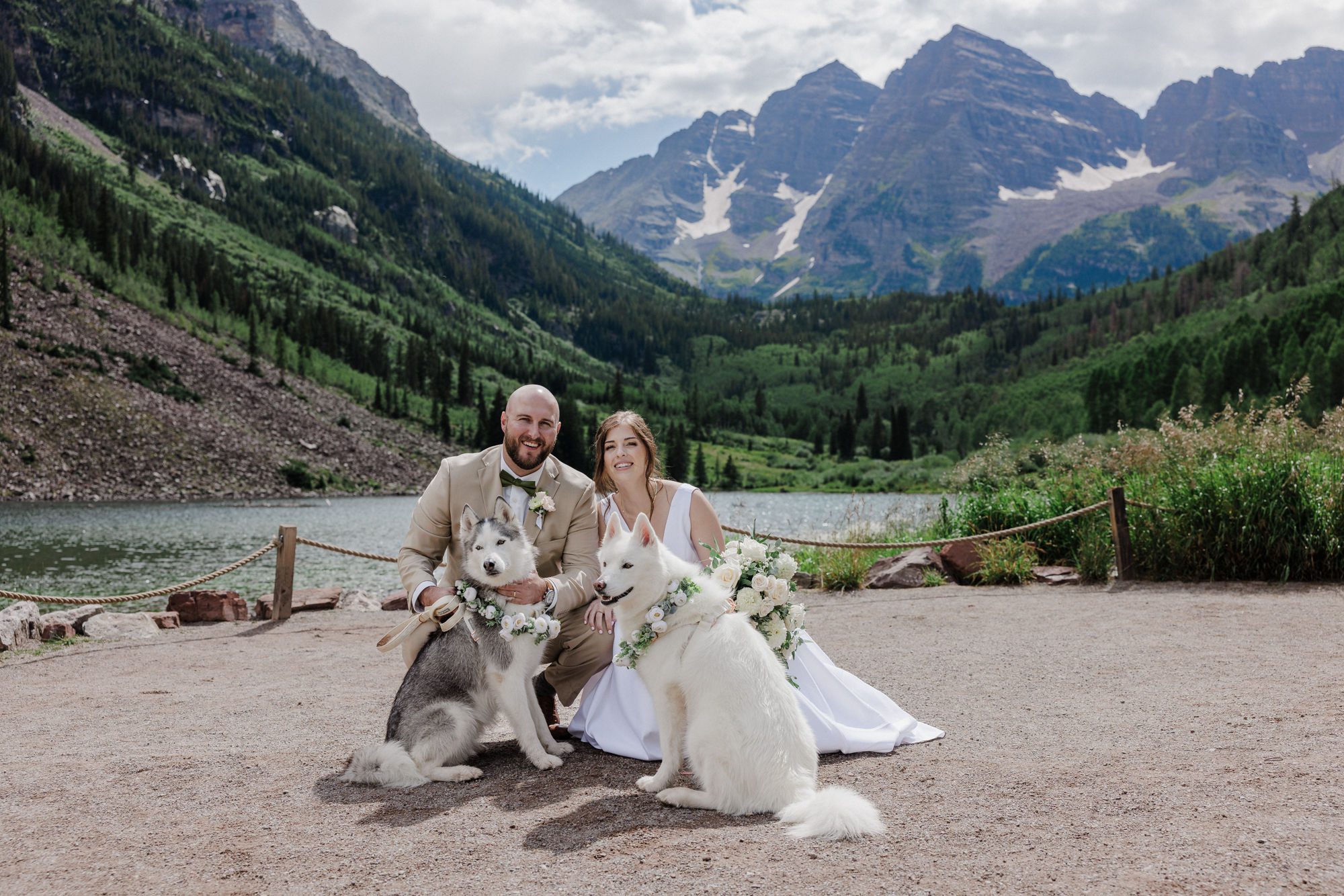 bride and groom lean down to take wedding photos with their pups