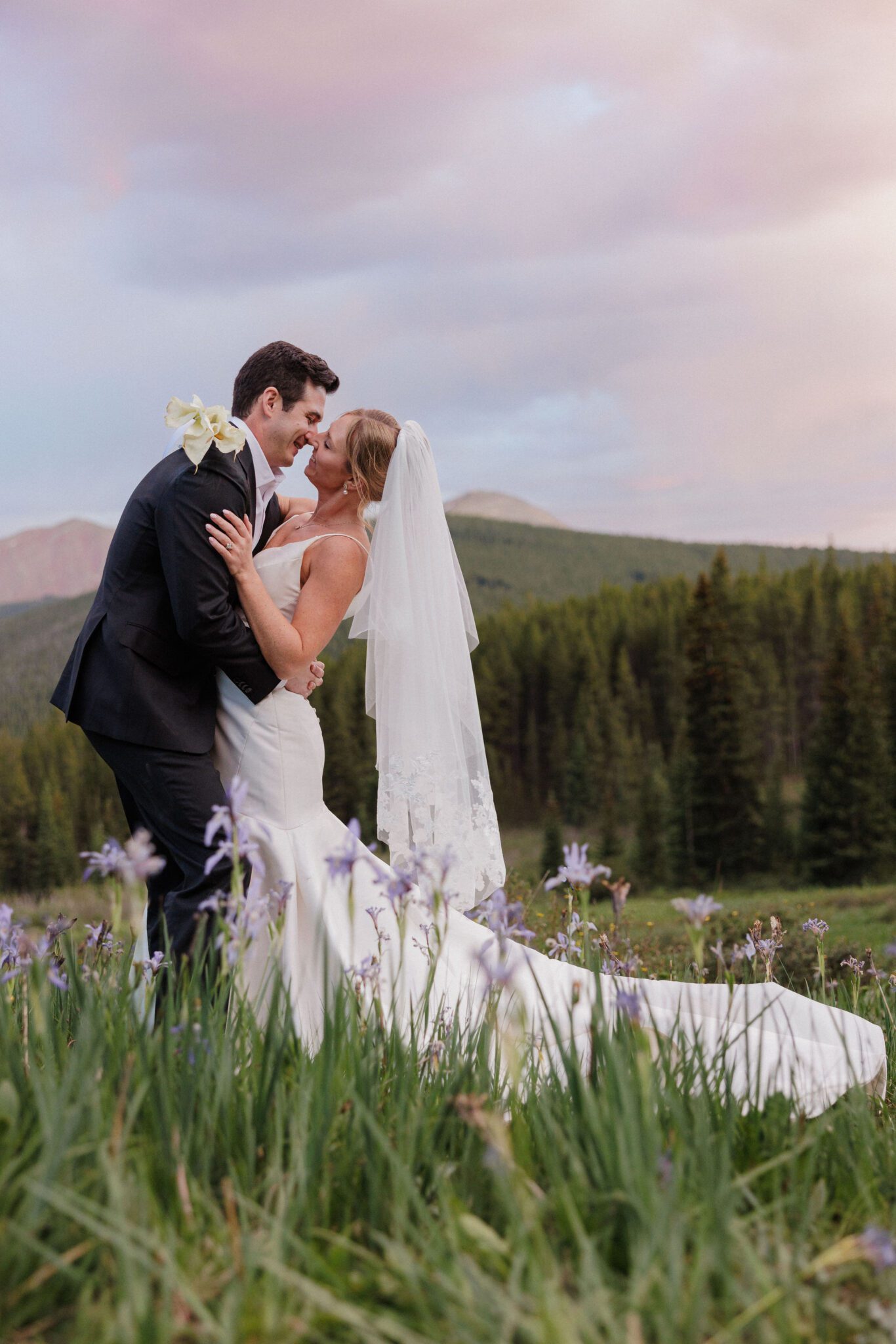 after choosing the adventure colorado elopement package, bride and groom kiss during sunset in the mountains. wildflowers in the foreground.