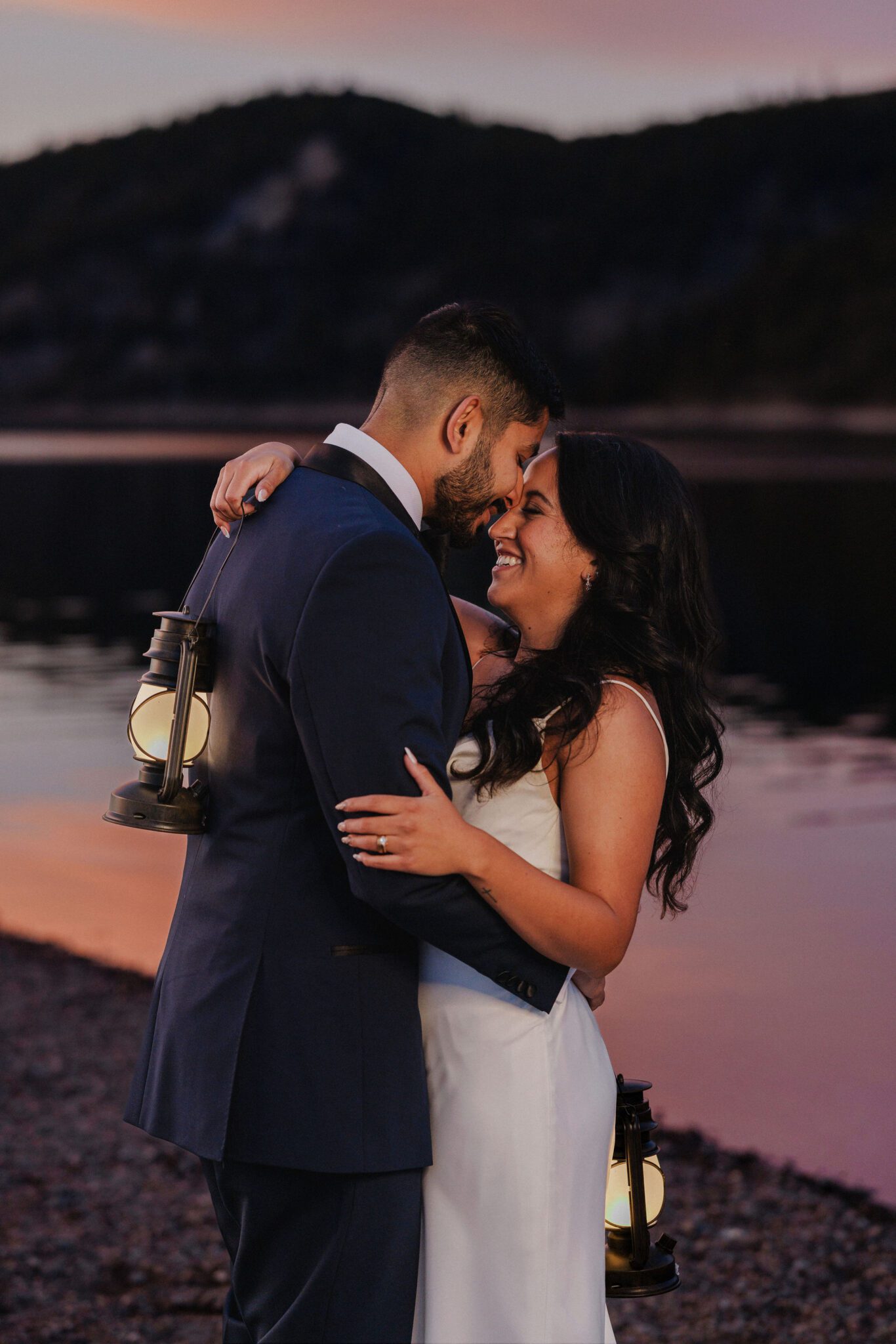bride and groom hold lanterns at take elopement photos during sunset by the lake