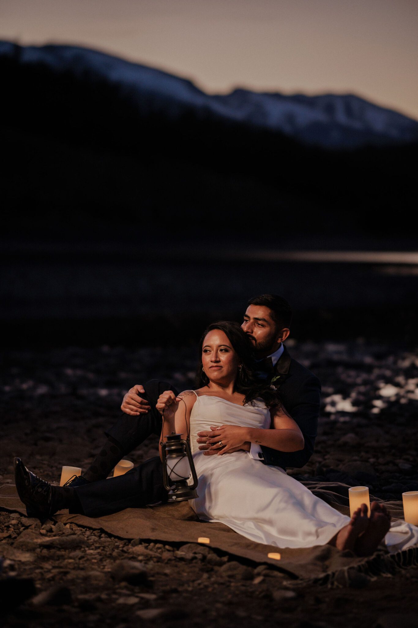 bride and groom sit on the ground with a blanket and candles during sunset wedding photos