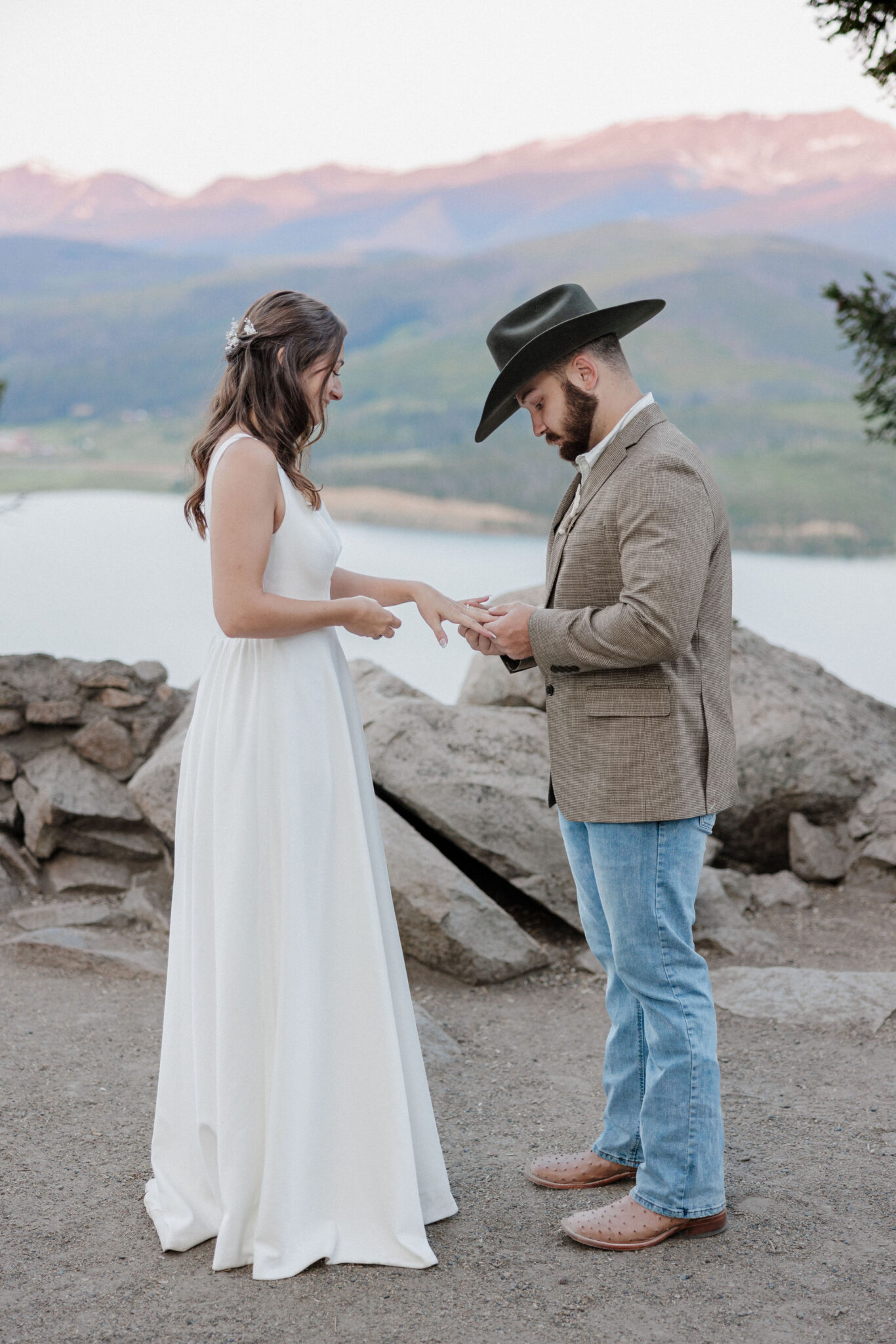 groom puts brides ring on her finger during lakeside wedding in the mountains of colorado