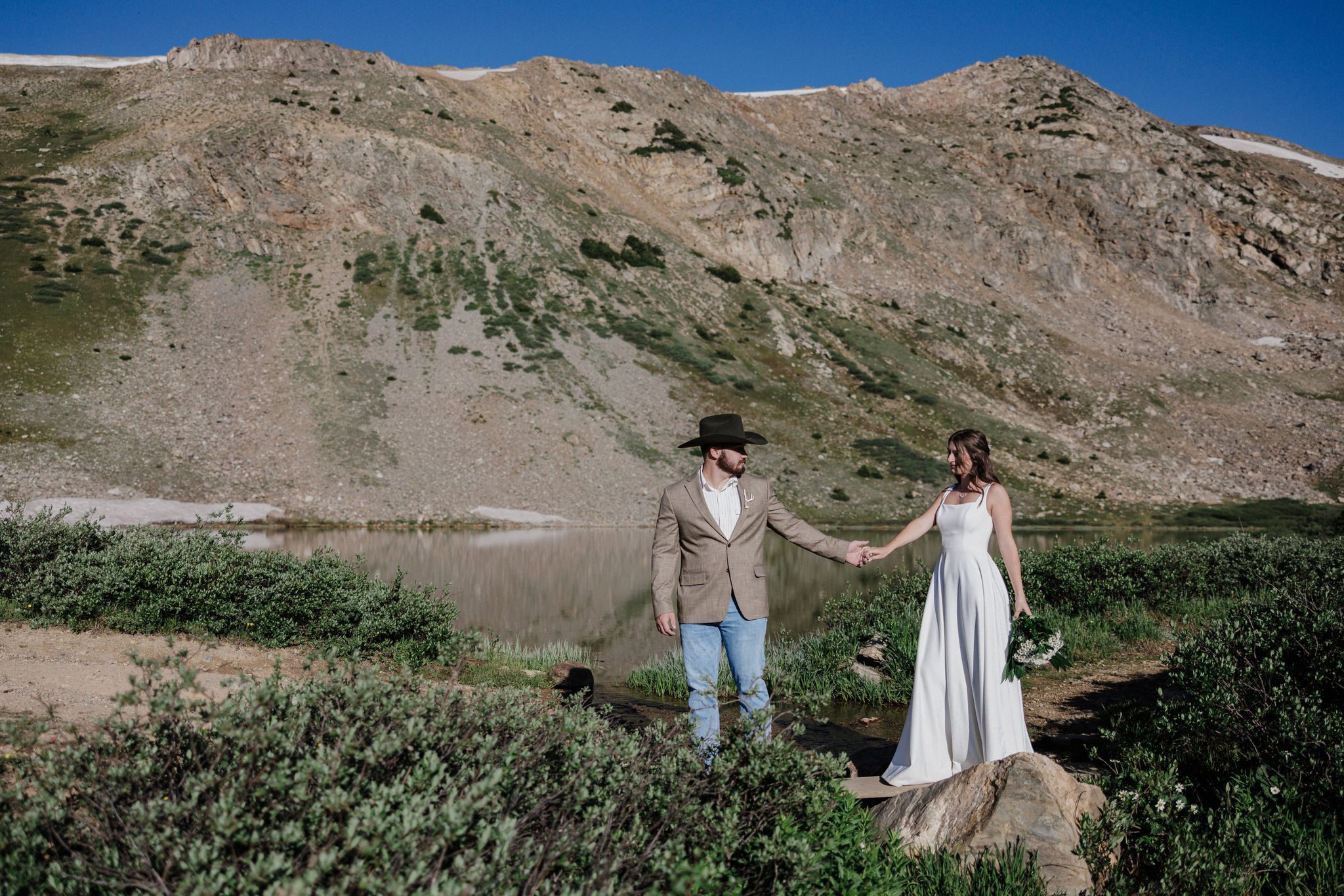 bride and groom hold hands as they walk around mountain lake during colorado elopement