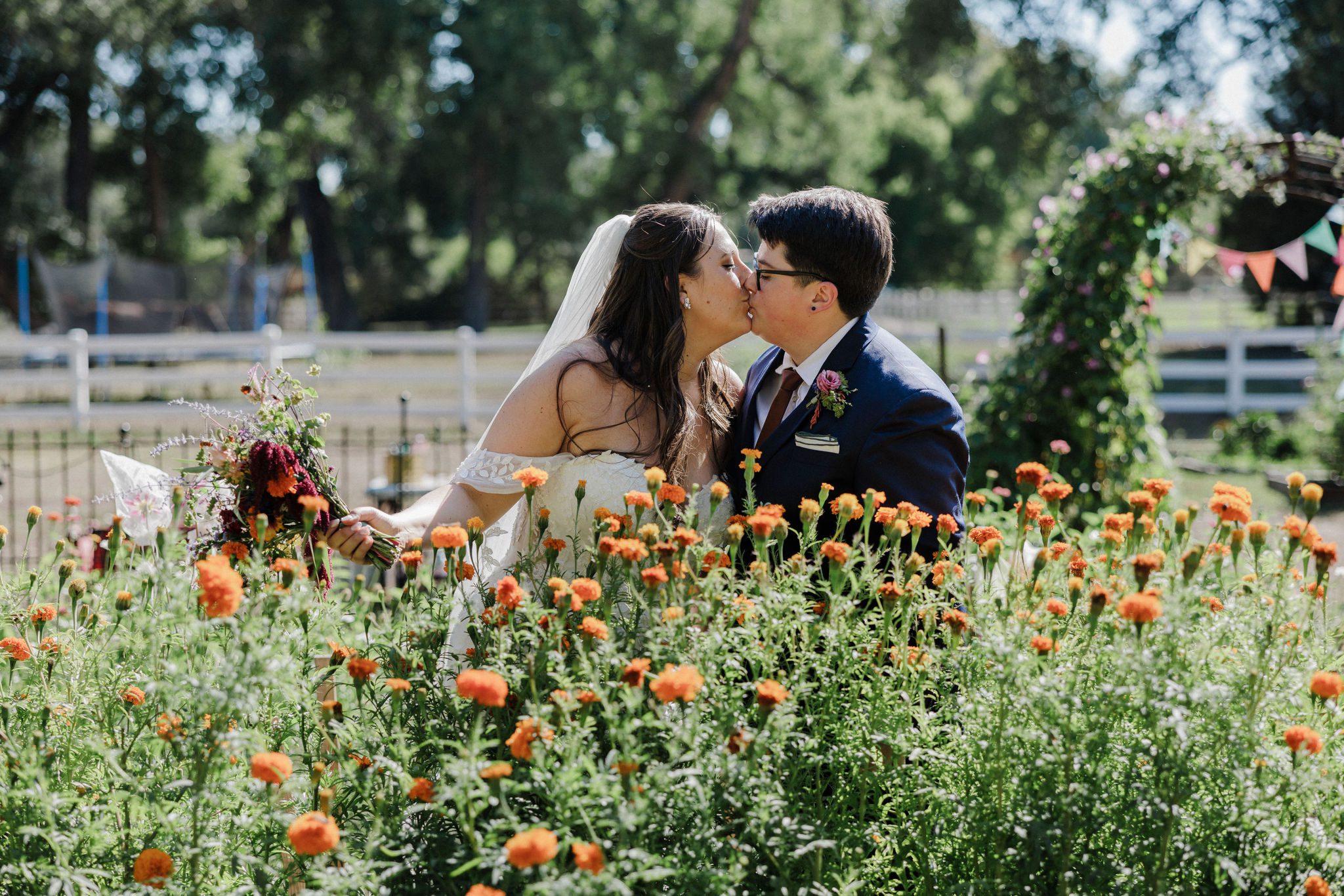 two brides kiss in front of field of orange wildflowers during summer microwedding