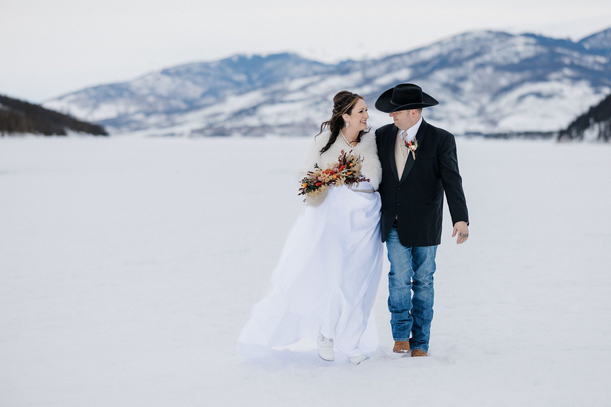 bride and groom walk on frozen lake during winter wedding in the mountains