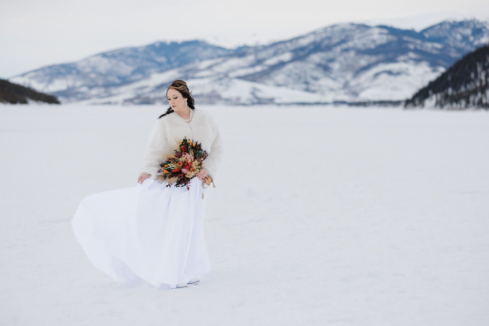 bride poses with floral bouquet during their mountain lake wedding in colorado