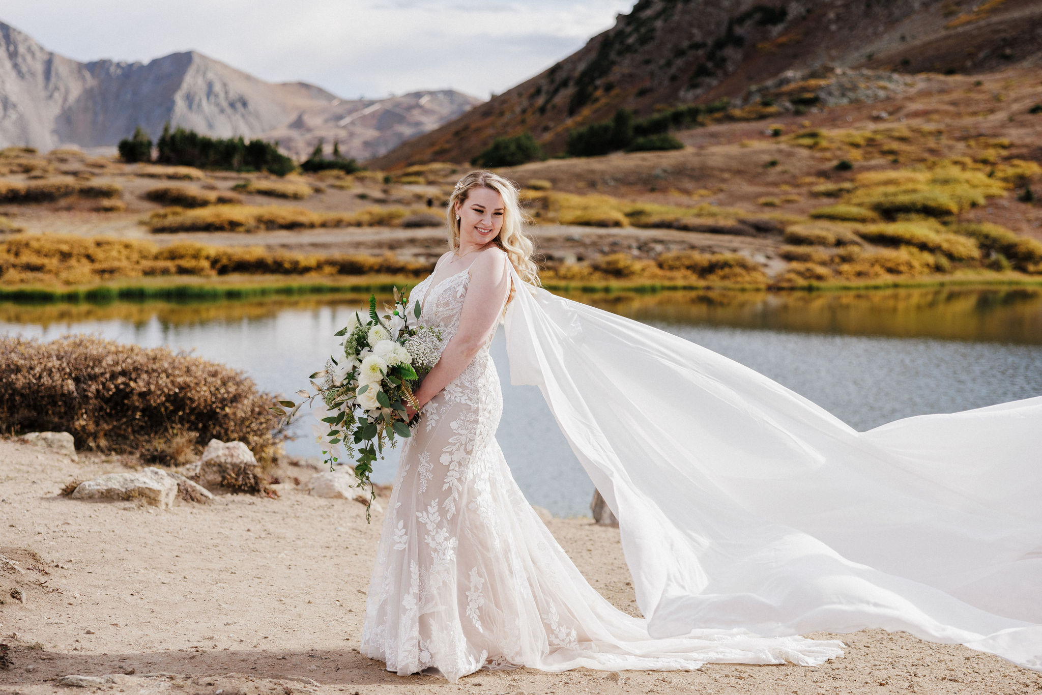 bride poses for photographer during colorado mountain lake wedding at pass lake