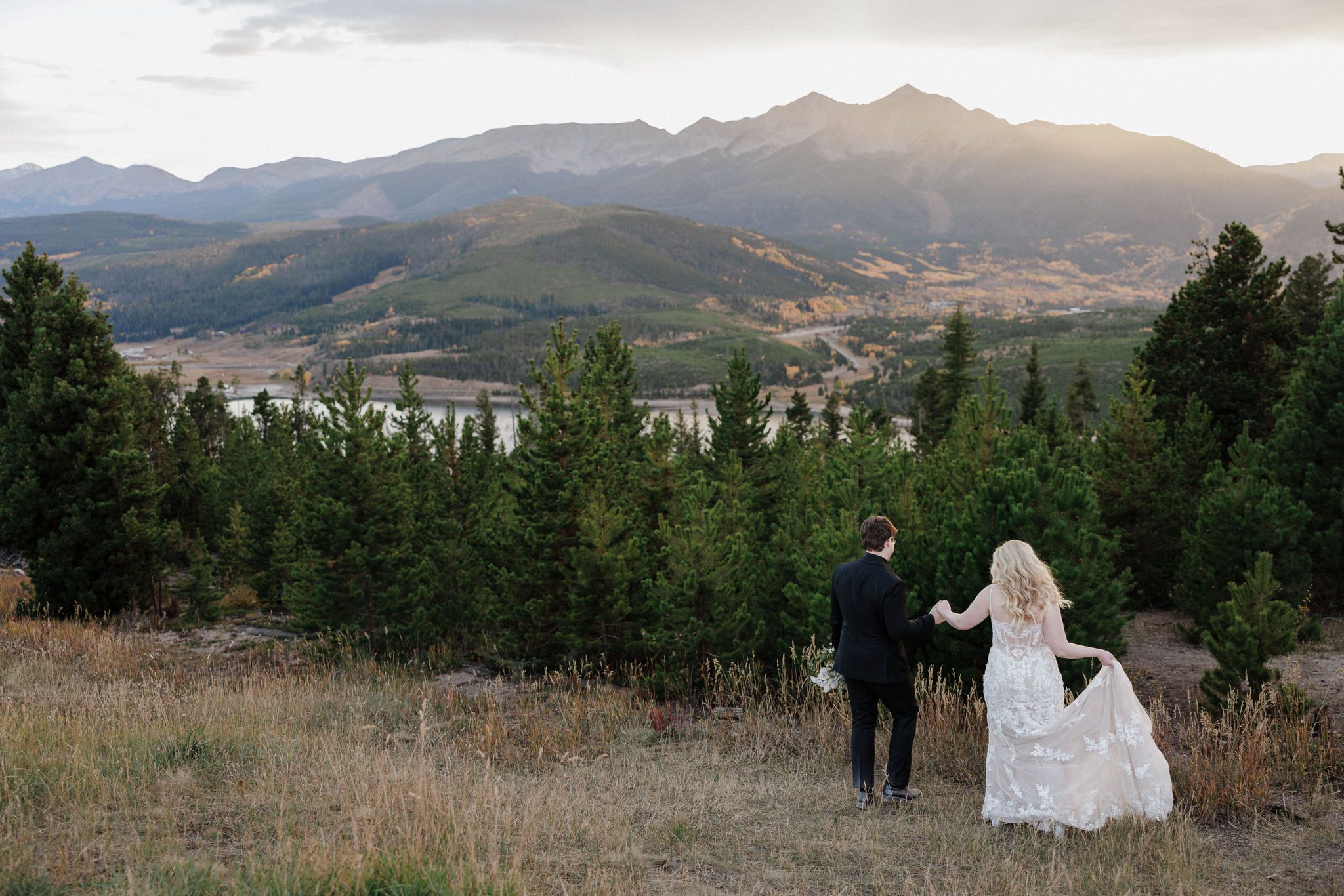 bride and groom hold hands and walk down hill in breckenridge during their colorado mountain lake wedding