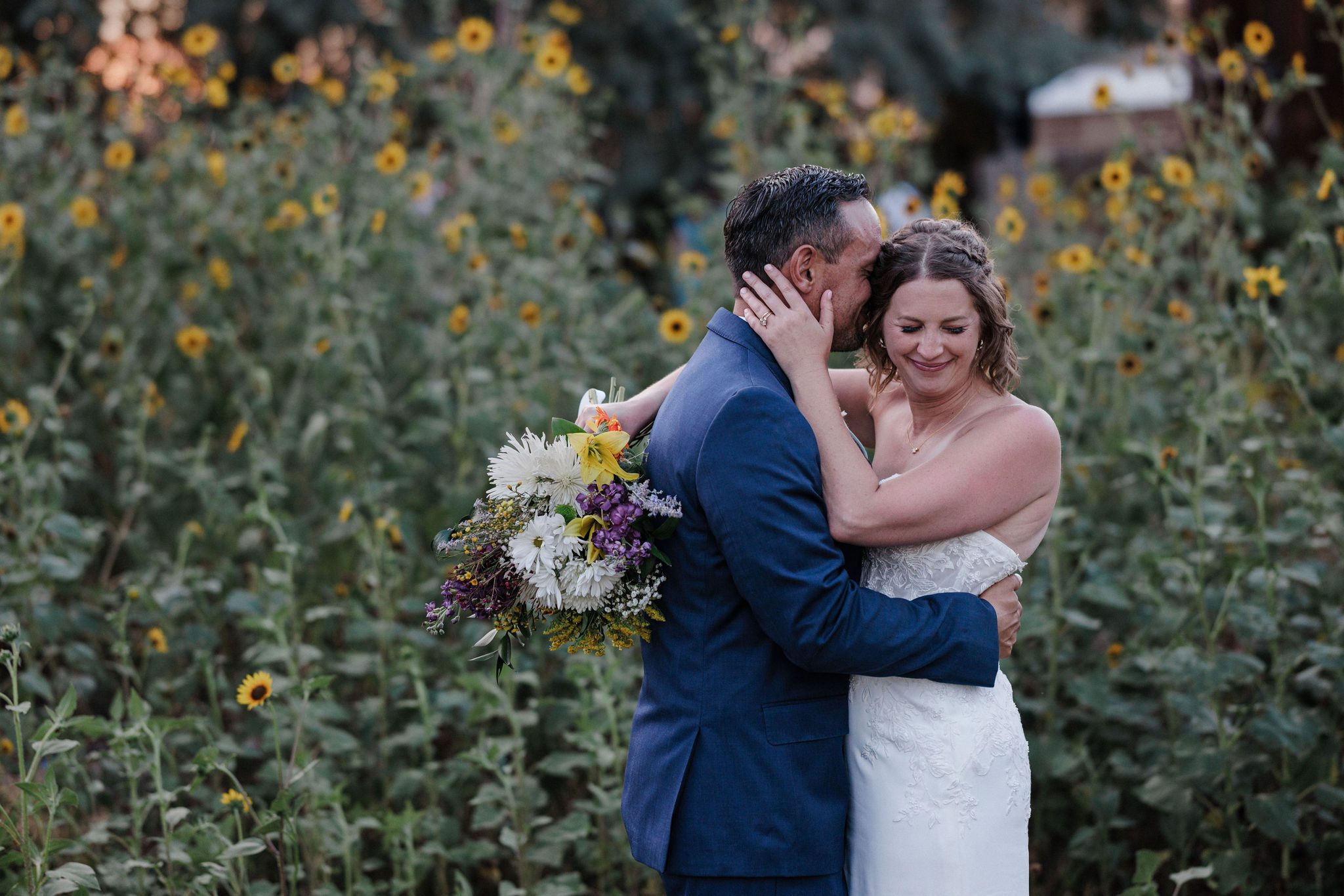 bride and groom dance and smile at colorado summer wedding venue, beside field of wildflowers