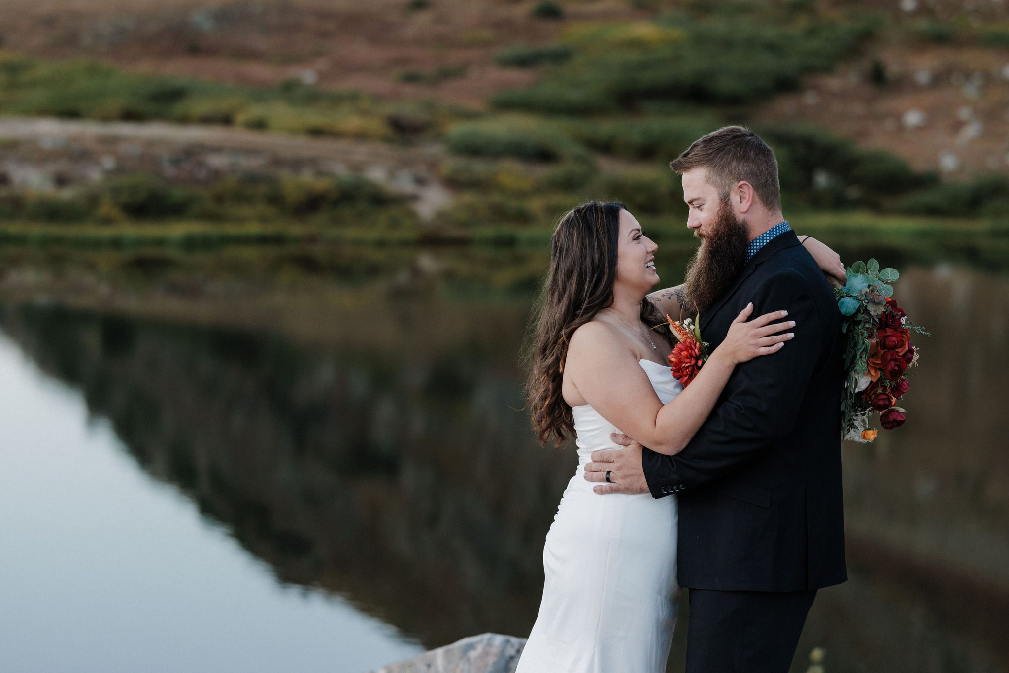 bride and groom smile at each other while taking wedding photos during their mountain lake wedding in breckenridge