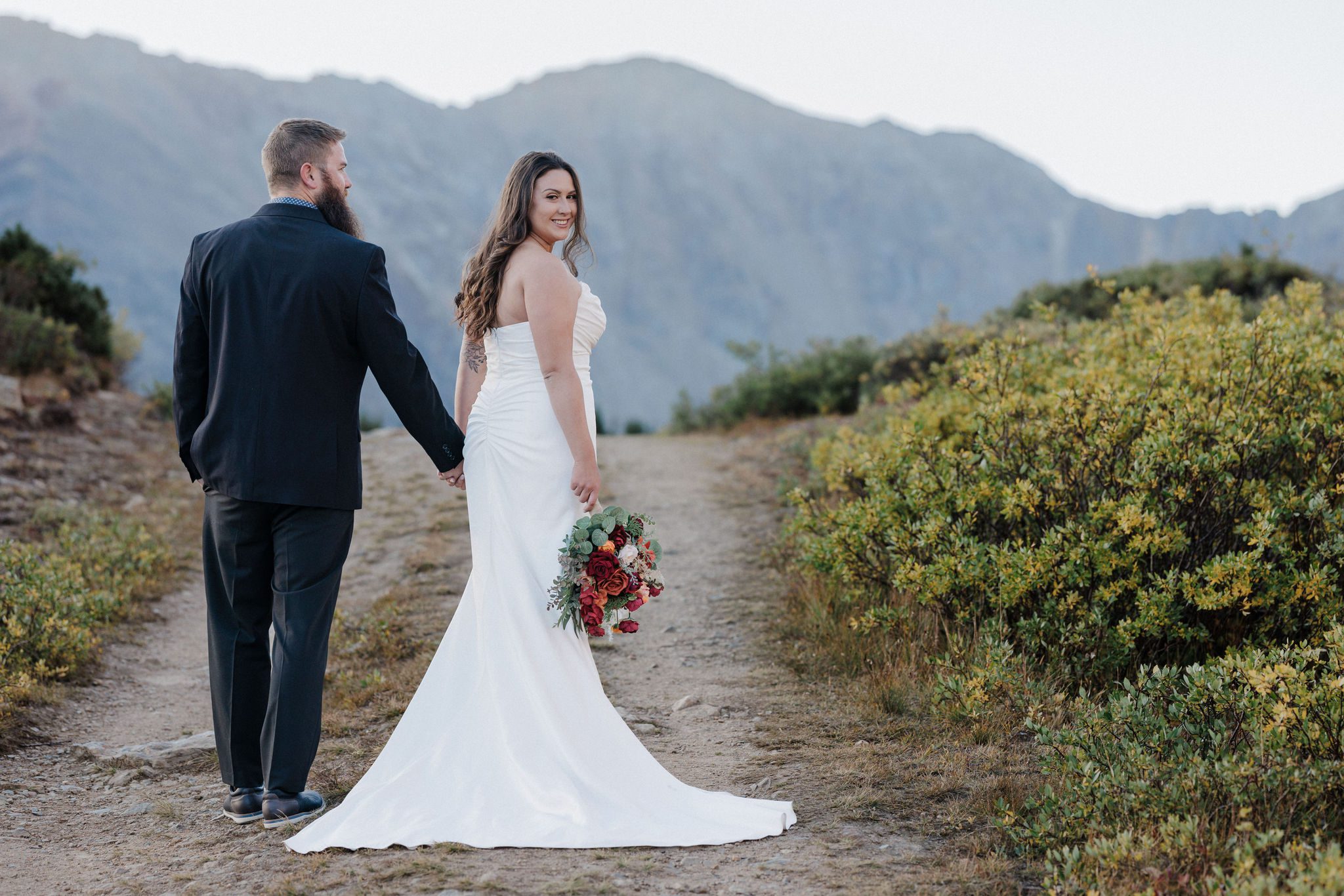 bride and groom hold hands and walk up a trail during colorado fall wedding in breckenridge